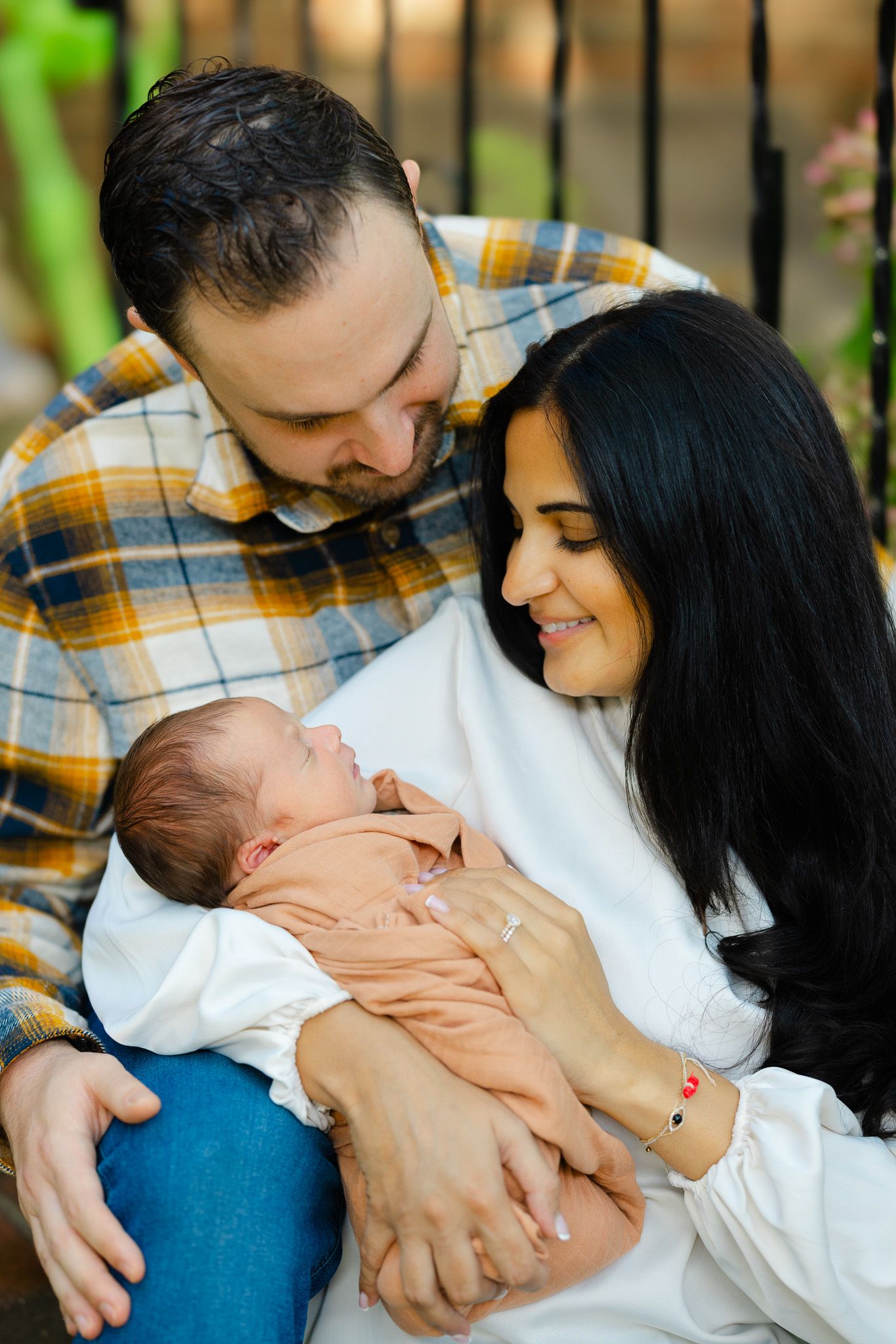 Parents share an intimate moment with their newborn baby while sitting together outdoors.