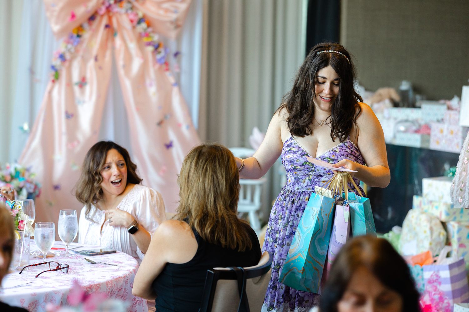 A group gathers at a pink-themed party with decorative elements and table settings in a bright indoor space.