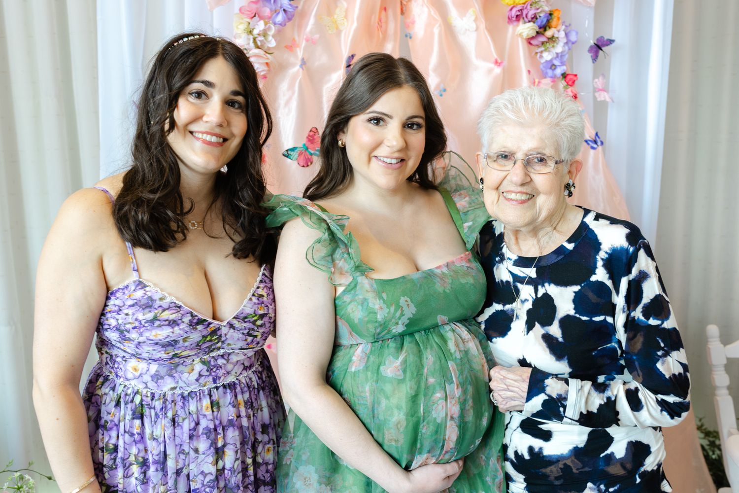 A group of people wearing floral and polka dot dresses pose together in a row for a formal event photo.