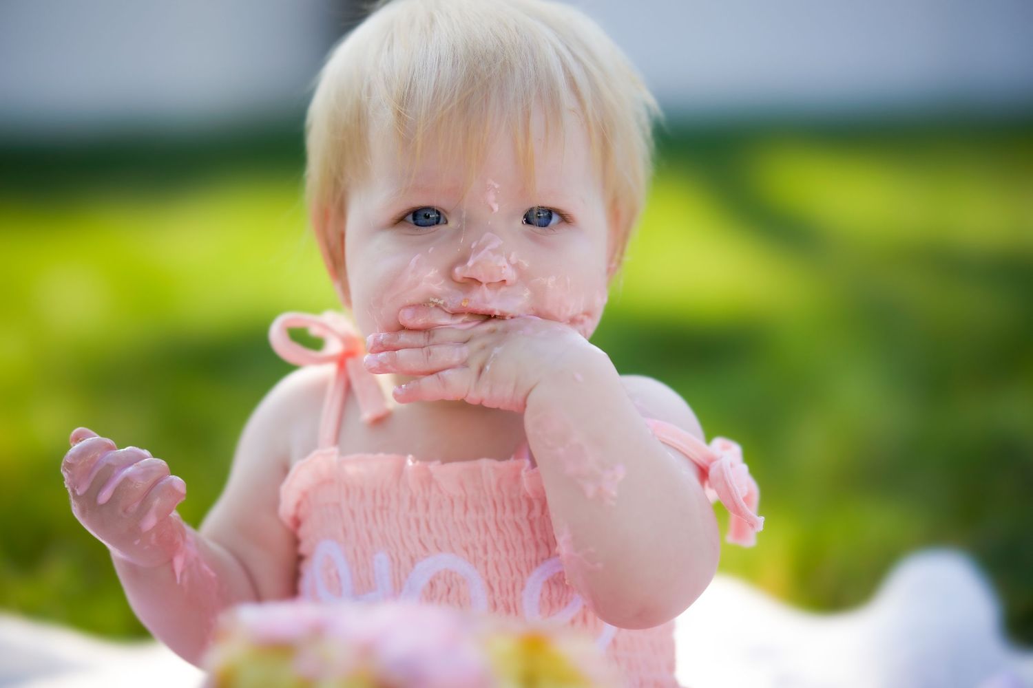 A young child wearing a pink sweater plays outdoors in a grassy area on a sunny day.