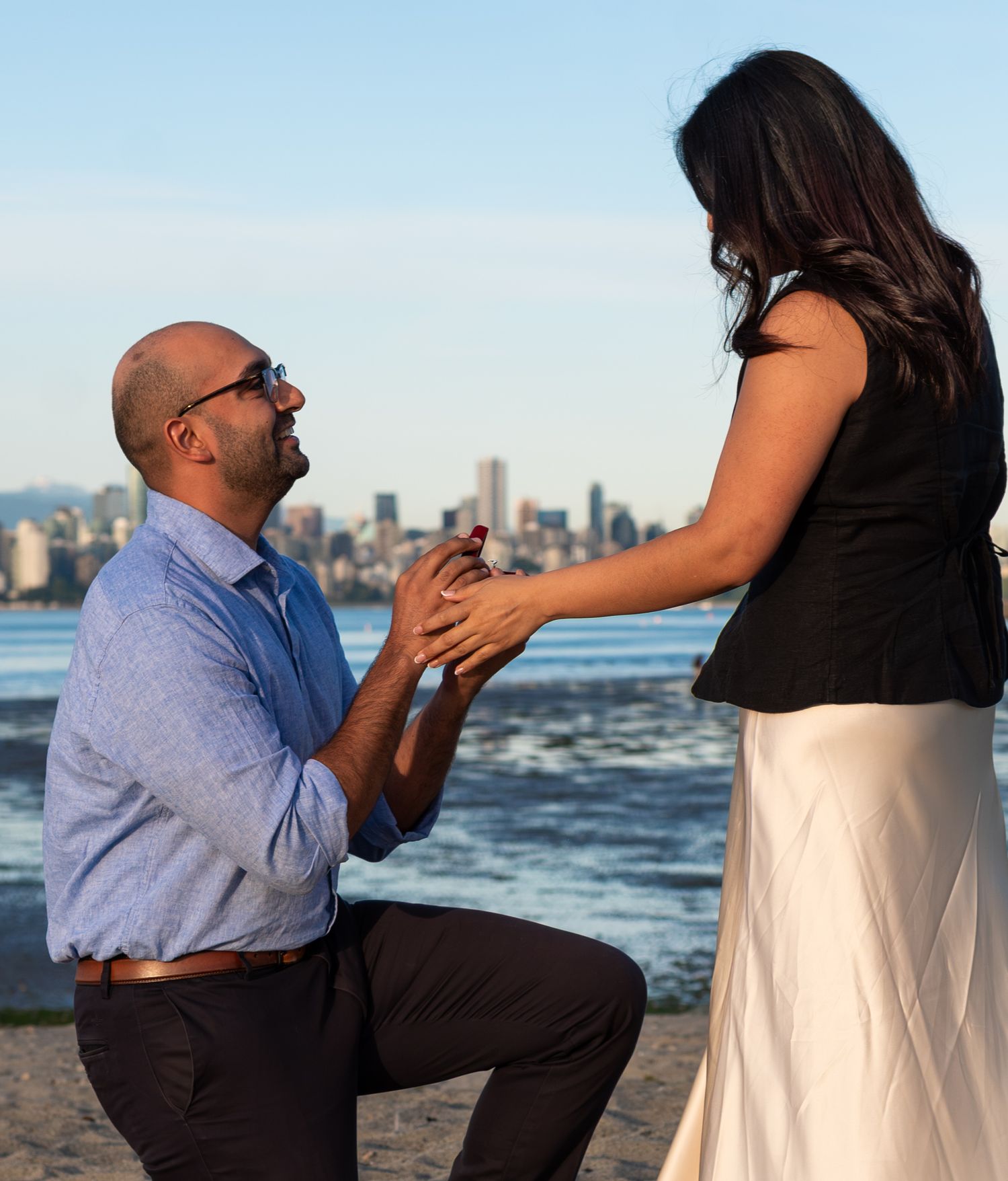 man proposing to woman on the beach with city view in the background