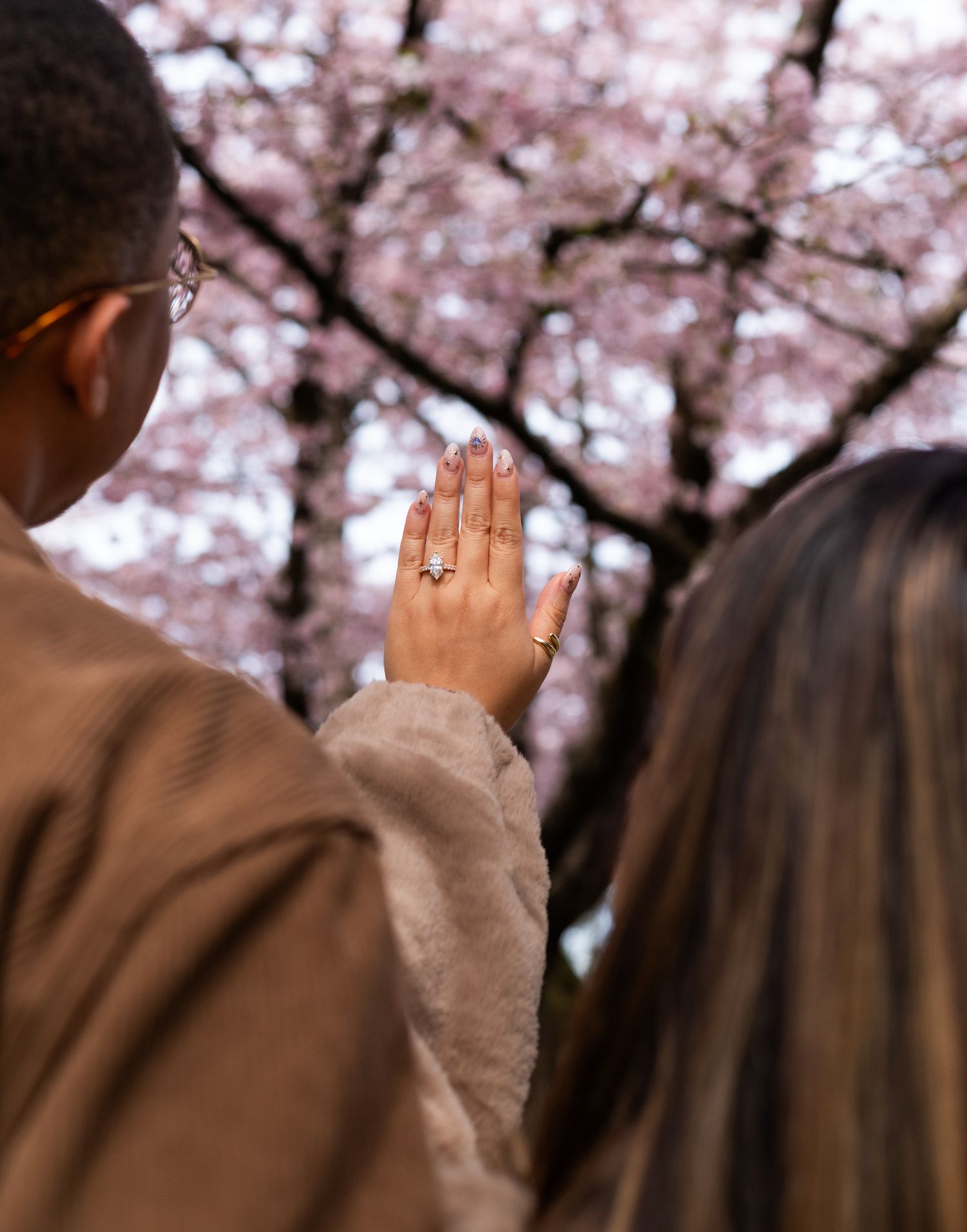 woman showing off ring against cherry blossom trees