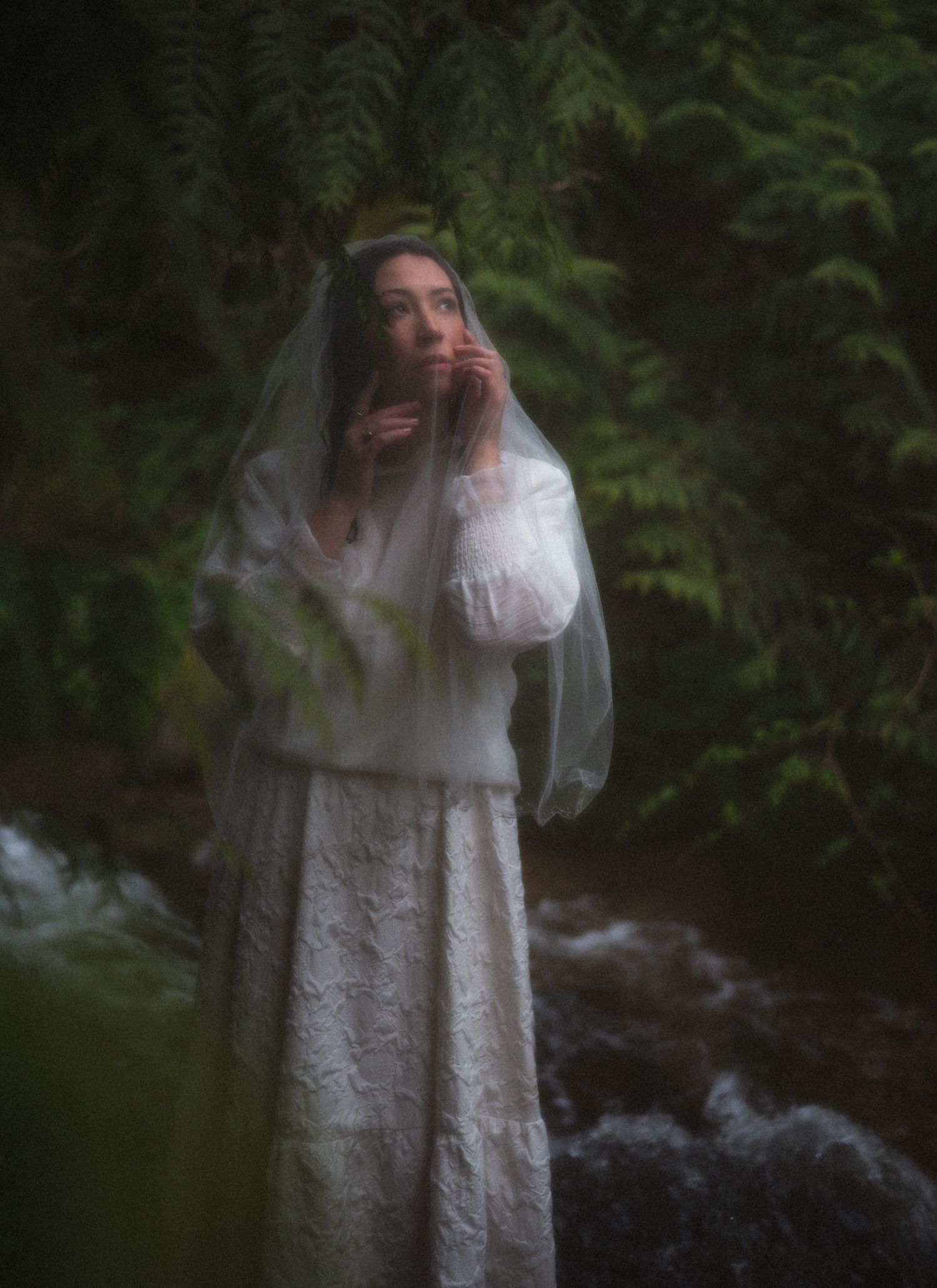 a woman posing under a tree by the water in nature.