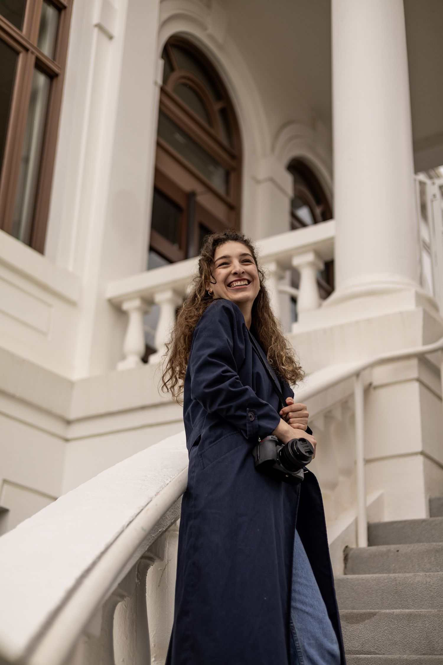 a woman with a camera leaning against a railing with a white building in the background