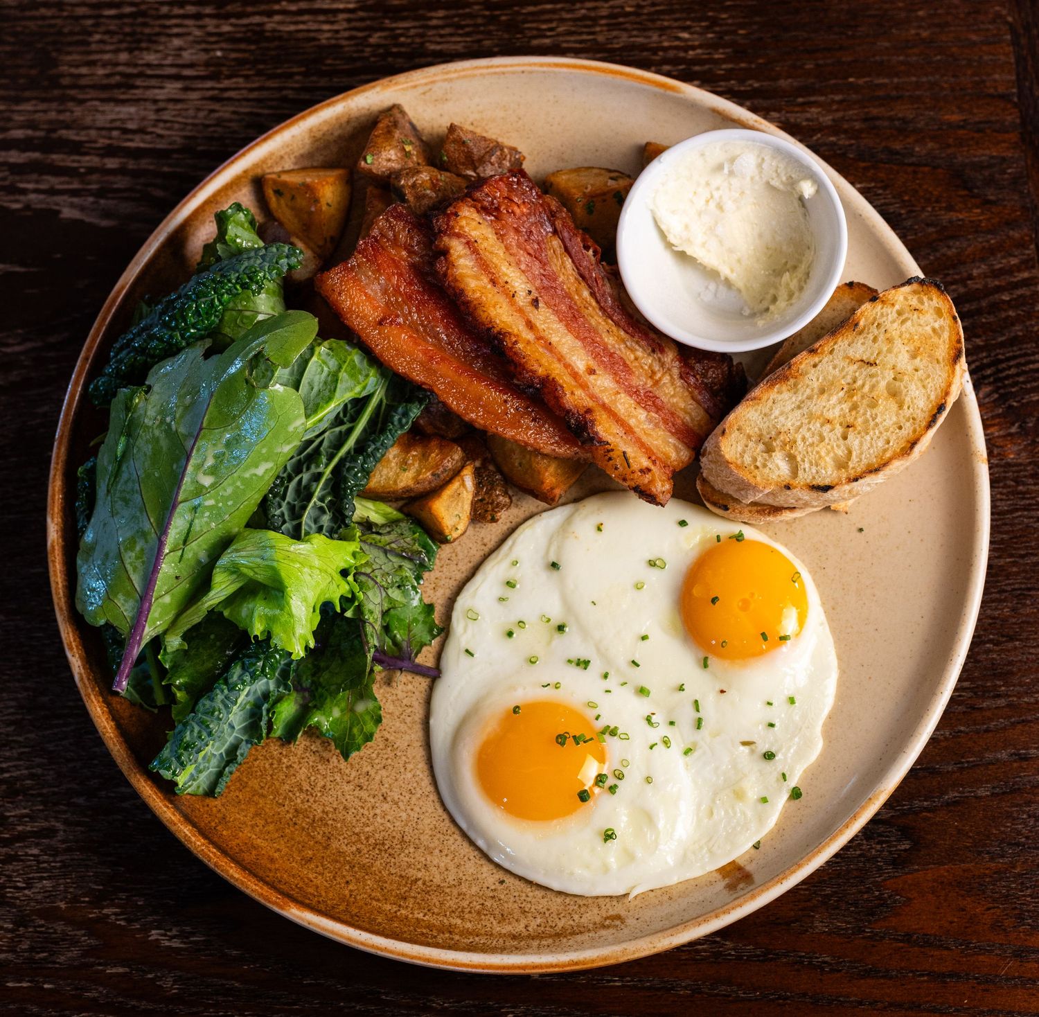 colourful photo of a breakfast plate with eggs bacon bread homemade butter and greens