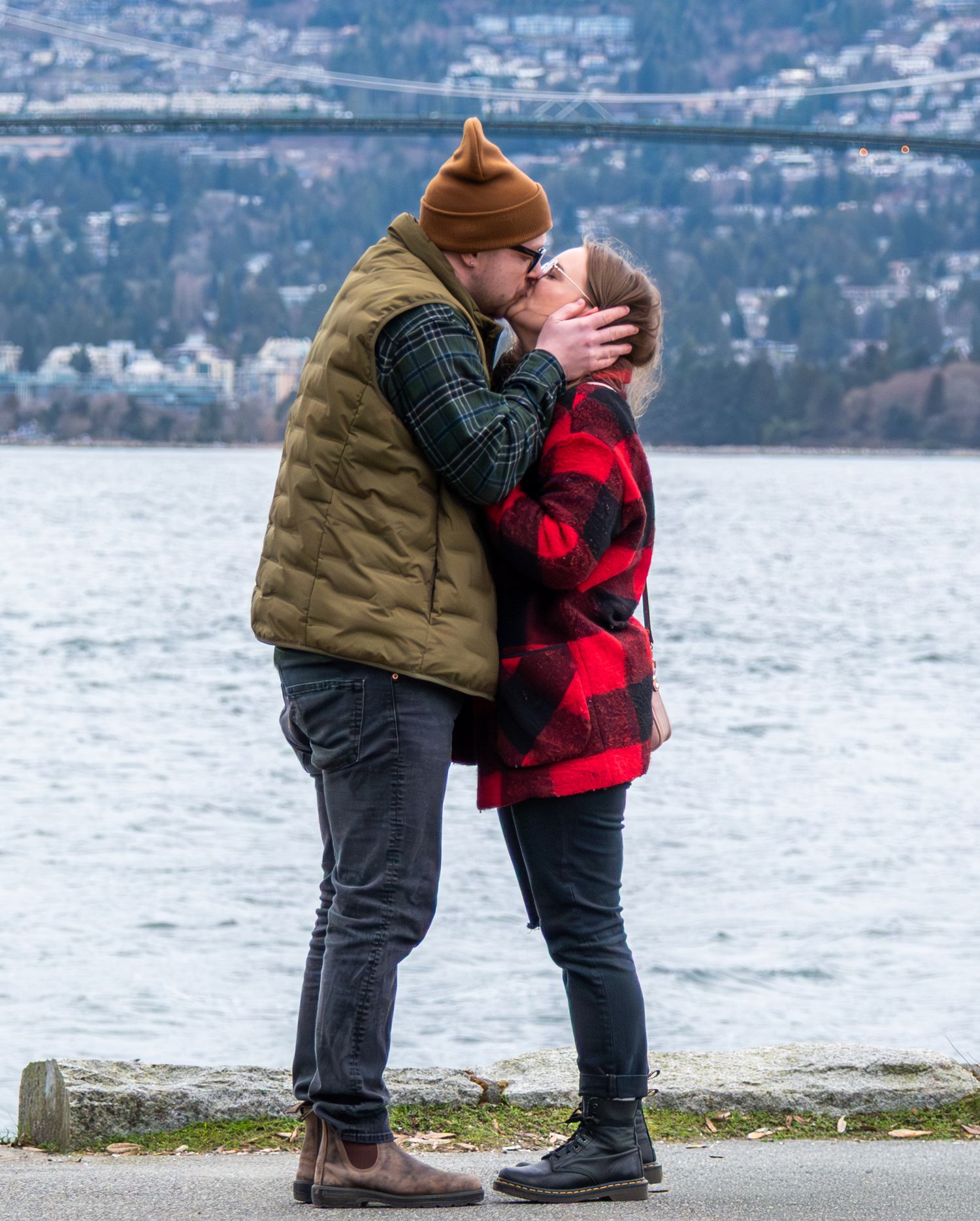 man kissing woman after proposal with lions gate bridge in background