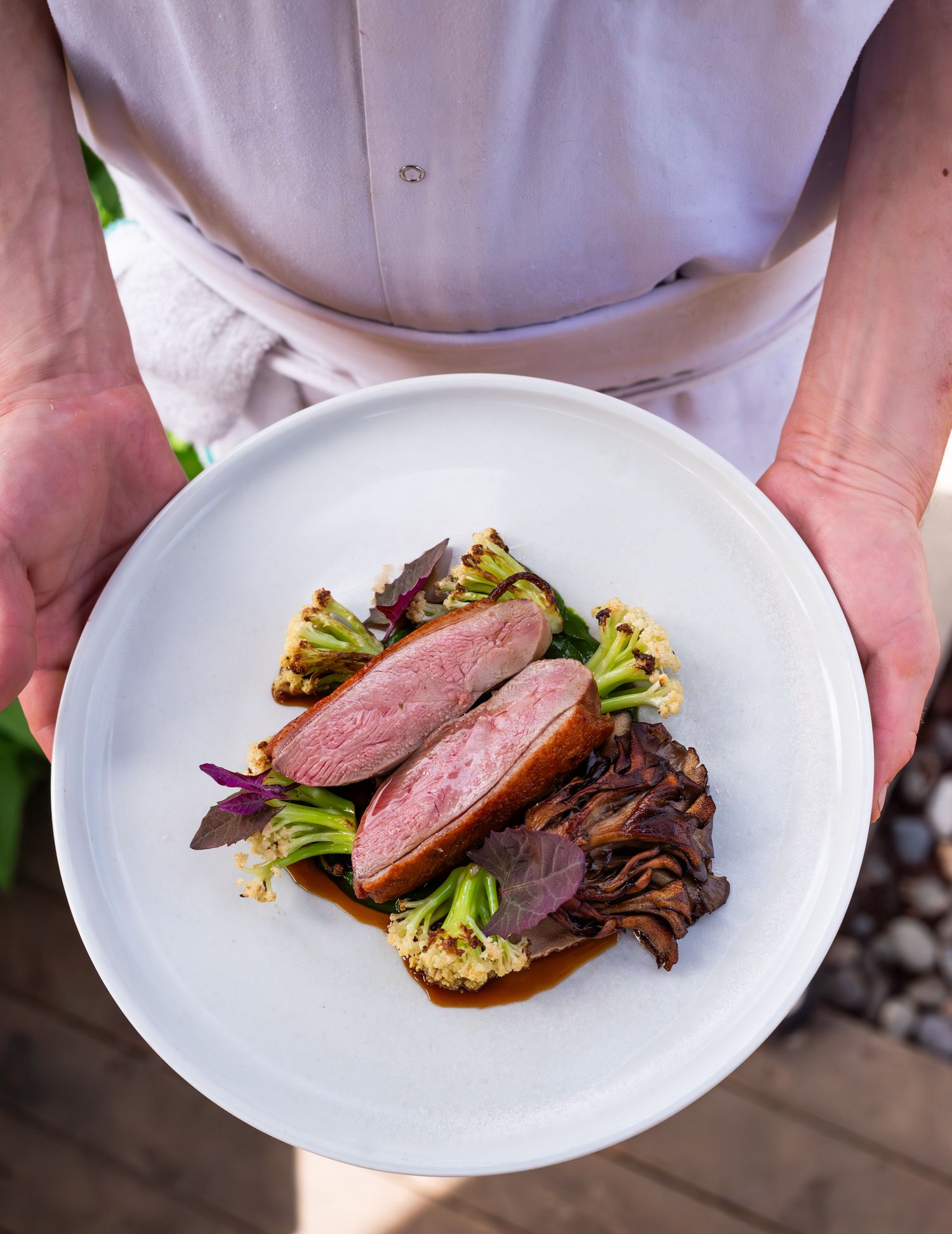photo of a man holding a dish with duck mushrooms and greens