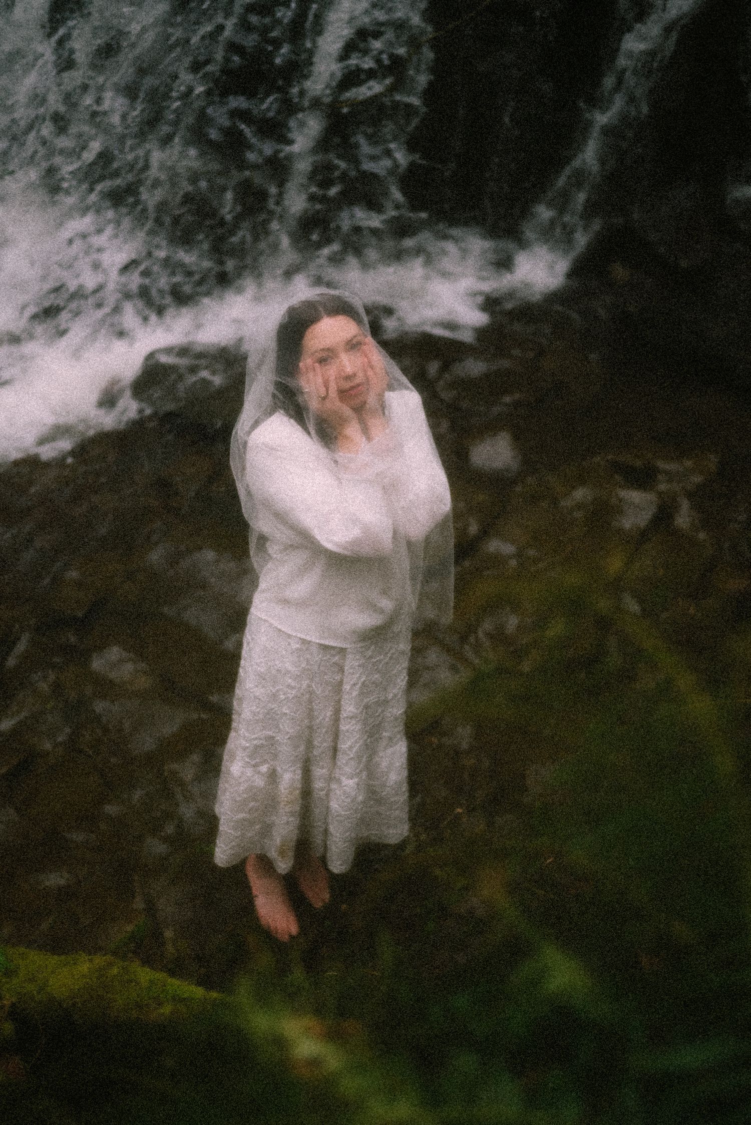 a woman posing standing near a waterfall in nature.