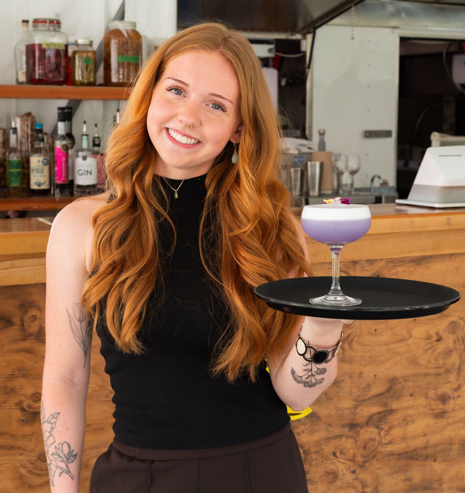 woman smiling holding a tray with a colourful drink on it