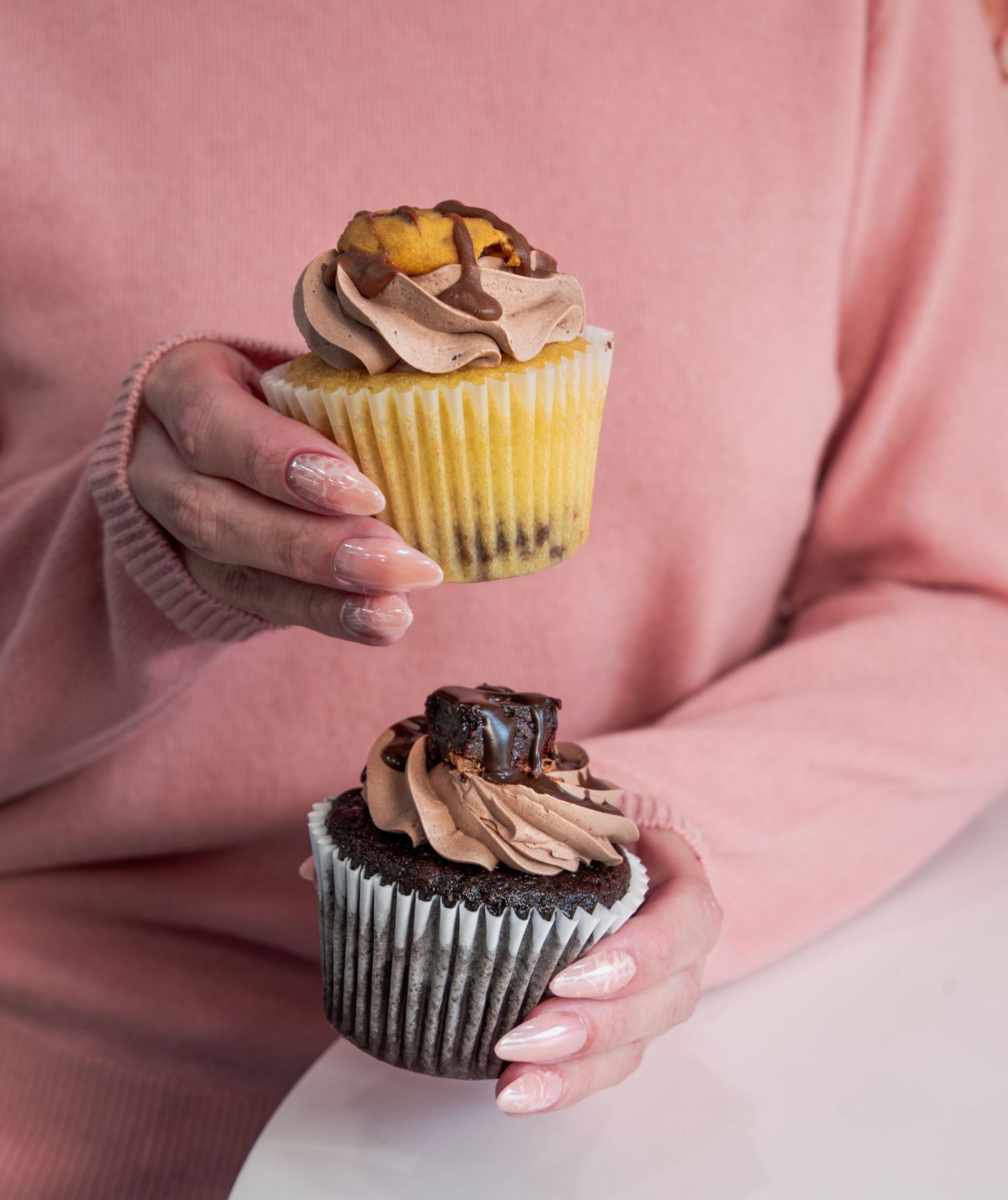 A close-up of two gourmet cupcakes held in manicured hands.