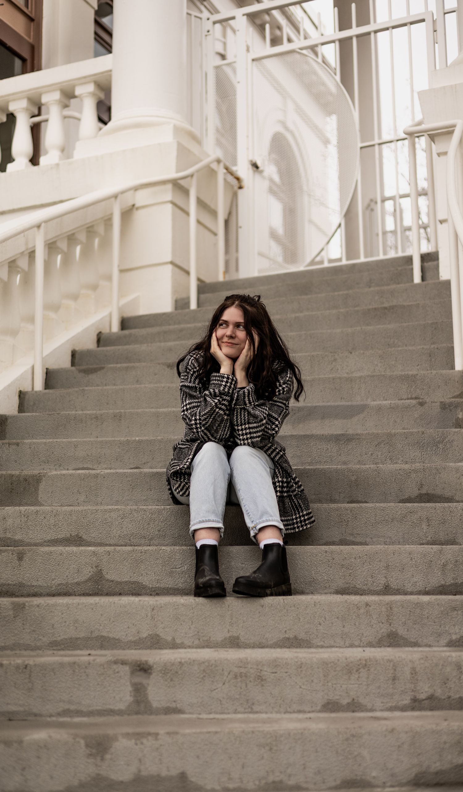 Woman Sitting on Outdoor Steps. Young woman with dark hair sitting on concrete steps outdoors, resting her chin on her hands.