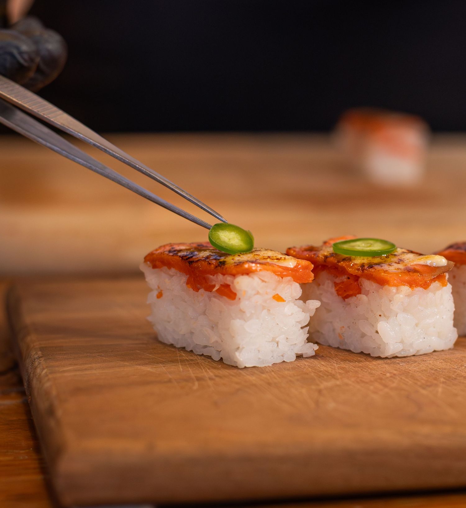 a jalapeno being placed on sushi with tweezers