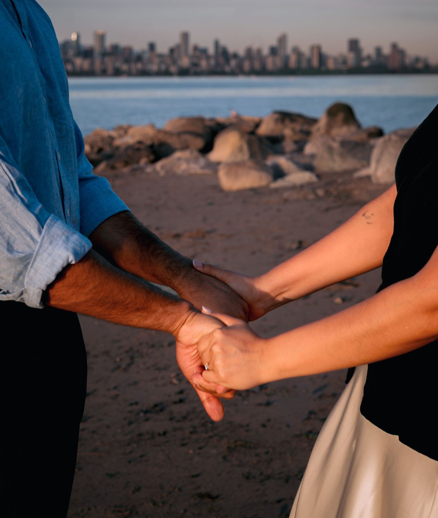 man and womans holding both hands on the beach with city view in the background