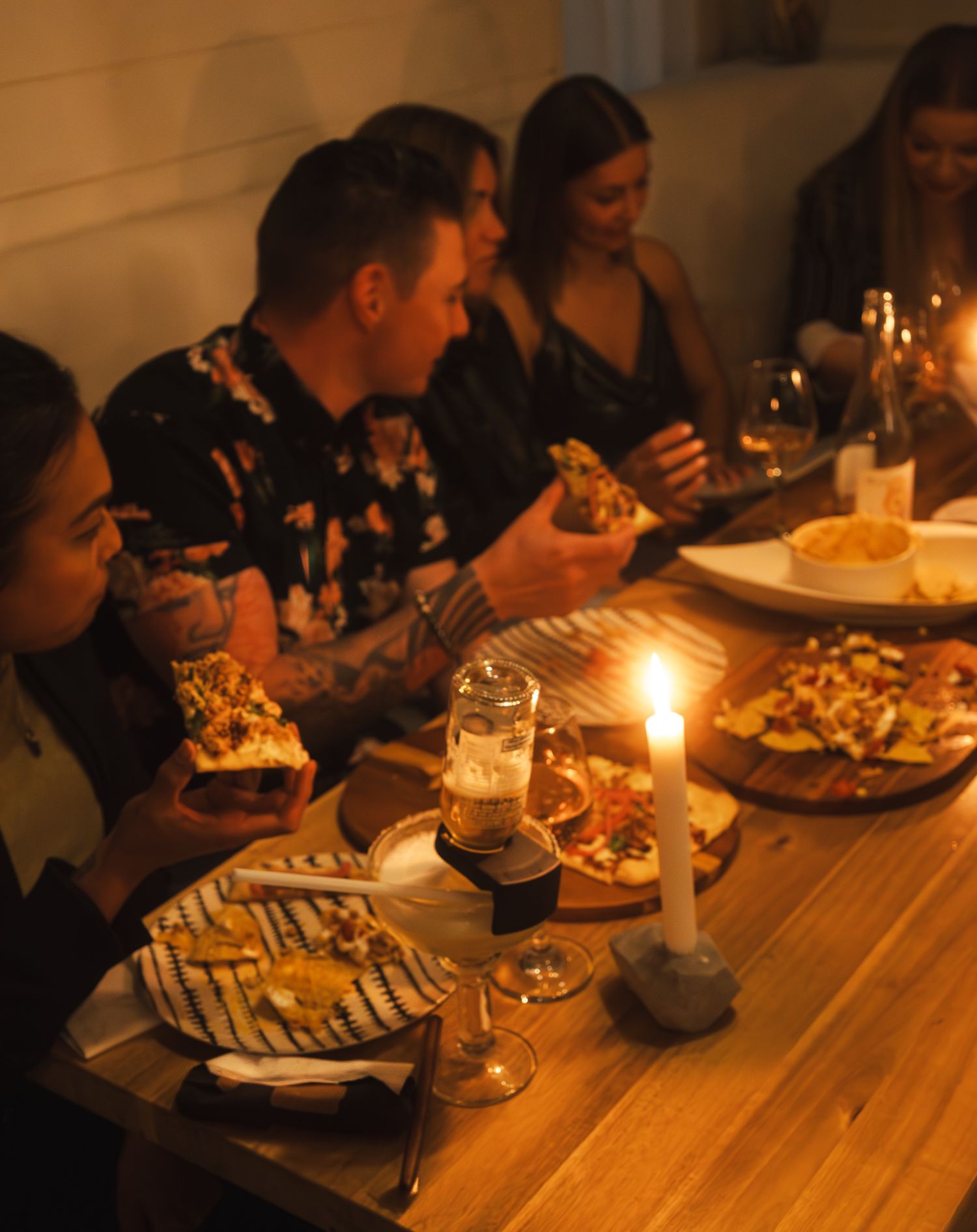 A group of friends enjoying pizza, nachos, and drinks by candlelight at a wooden table in an Abbotsford restaurant