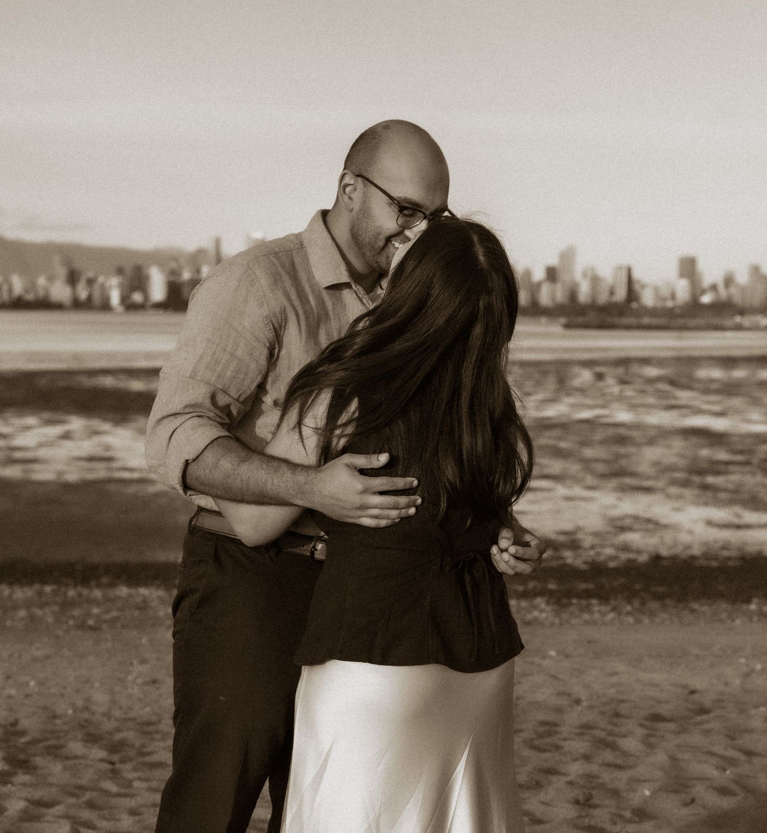 man kissing a woman on the beach with city view in background