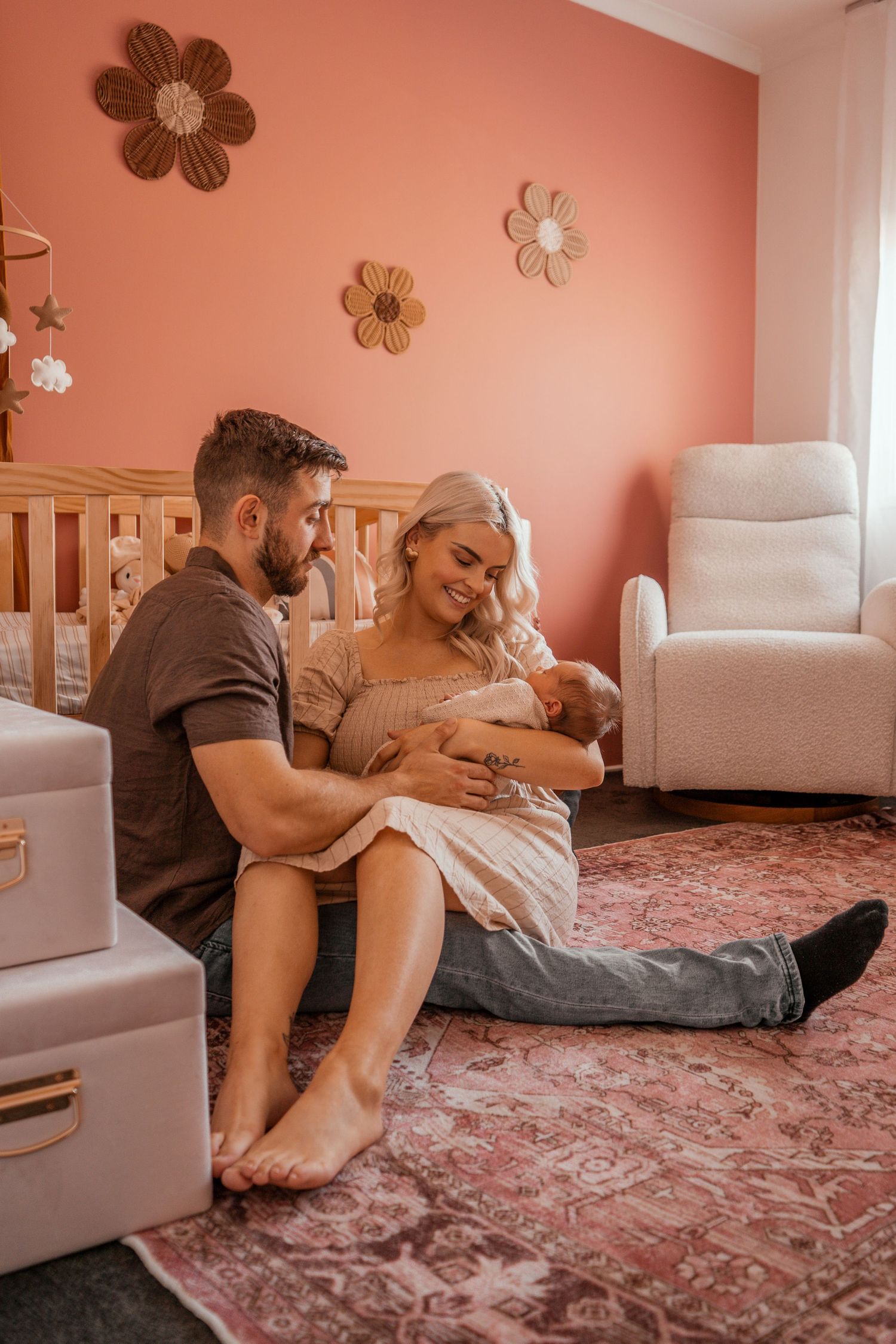 Couple relaxing together on pink carpeted floor in cozy nursery with white furniture and floral wall decals.