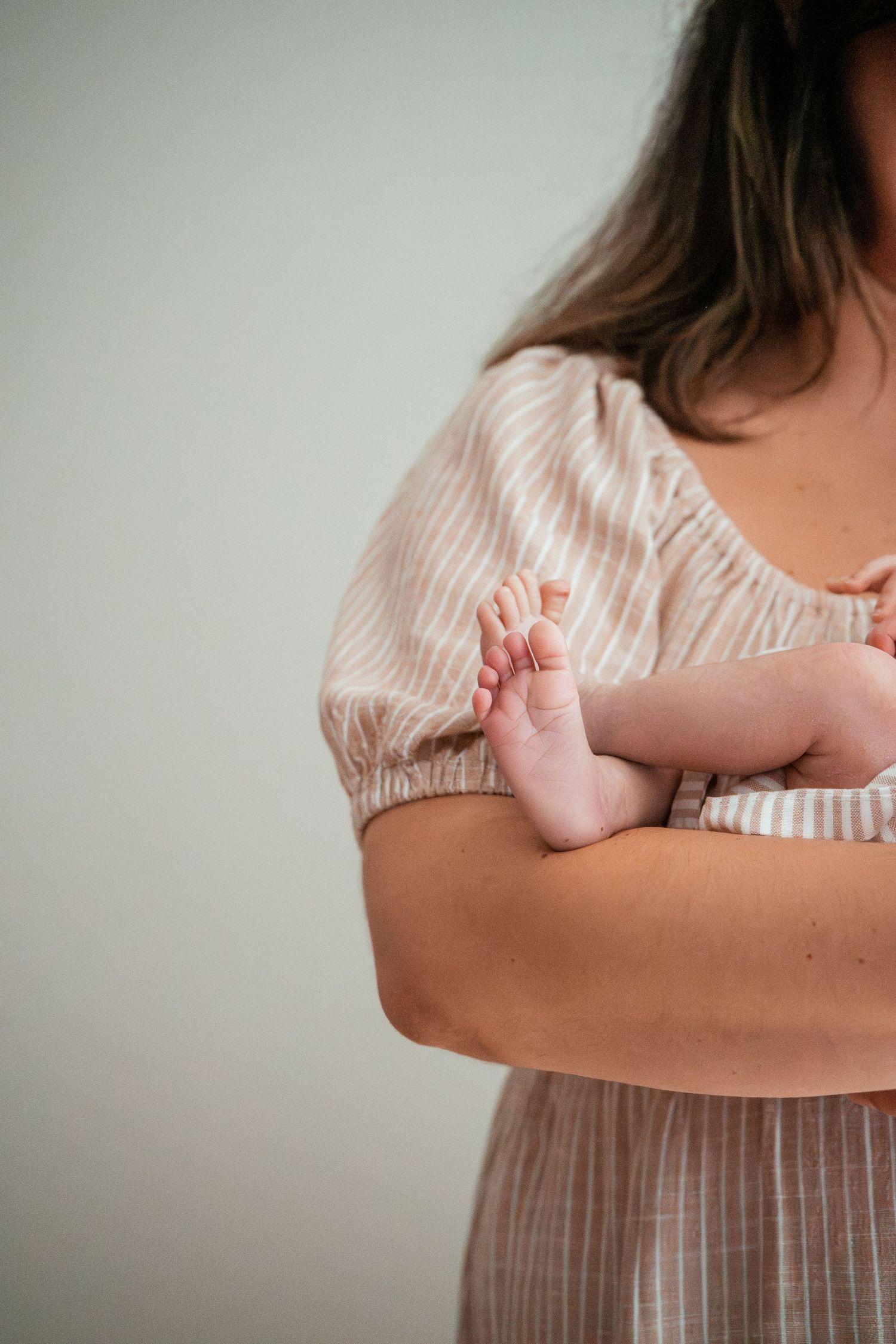 Close-up of tiny newborn baby foot being cradled against person wearing striped dress.