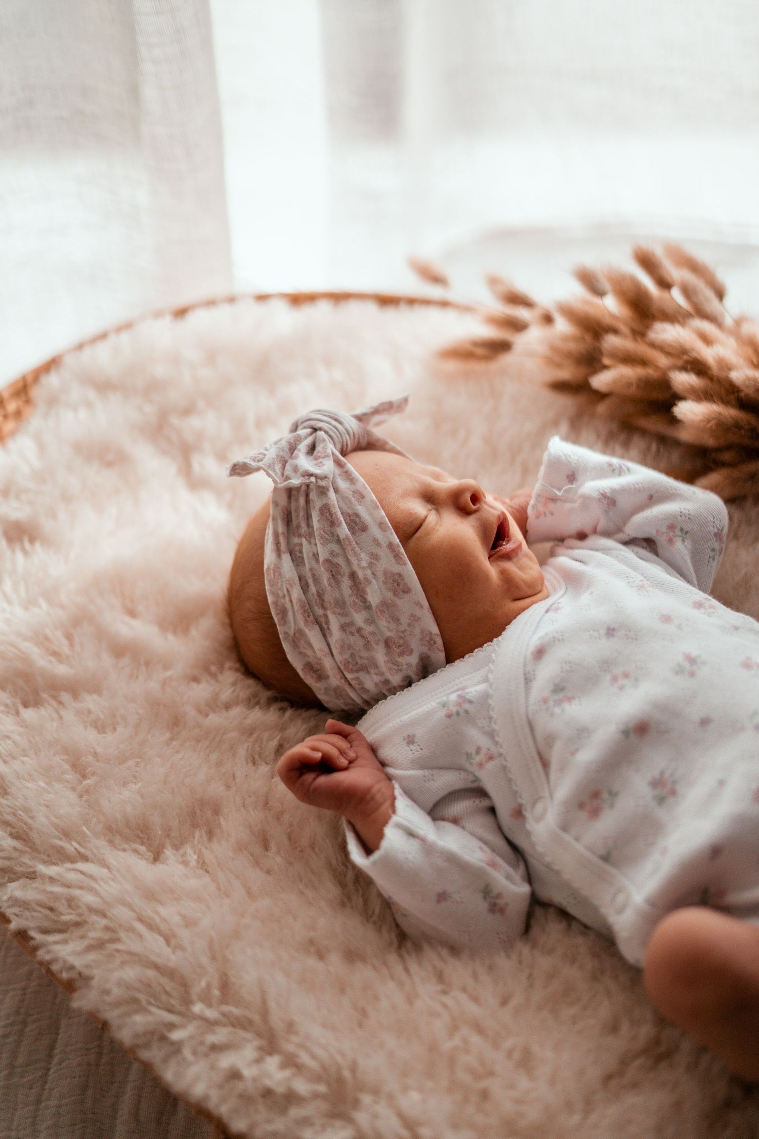 A sleeping newborn baby wearing a floral outfit rests peacefully on a plush pink blanket.
