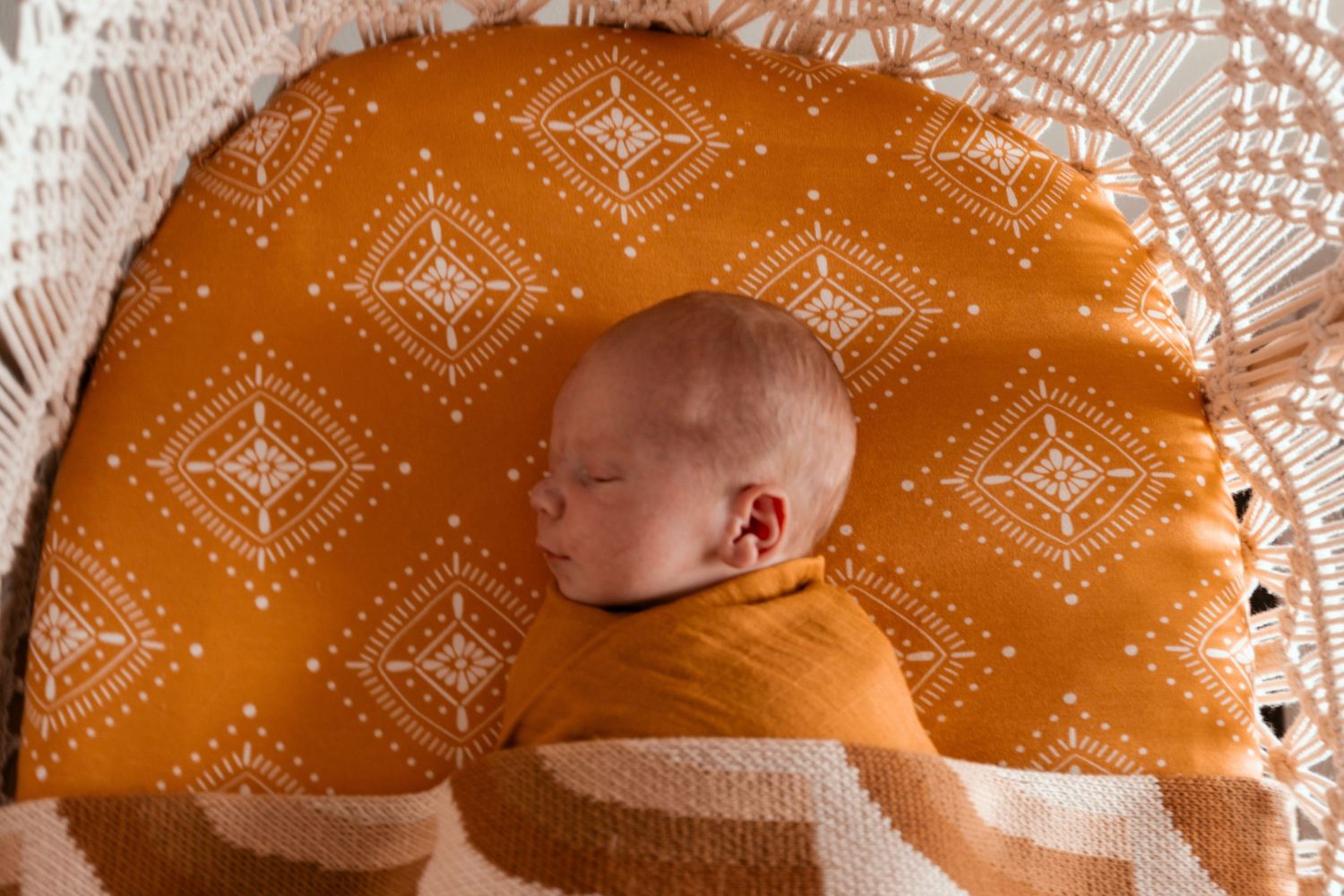Sleeping newborn on orange patterned blanket with white lace trim.
