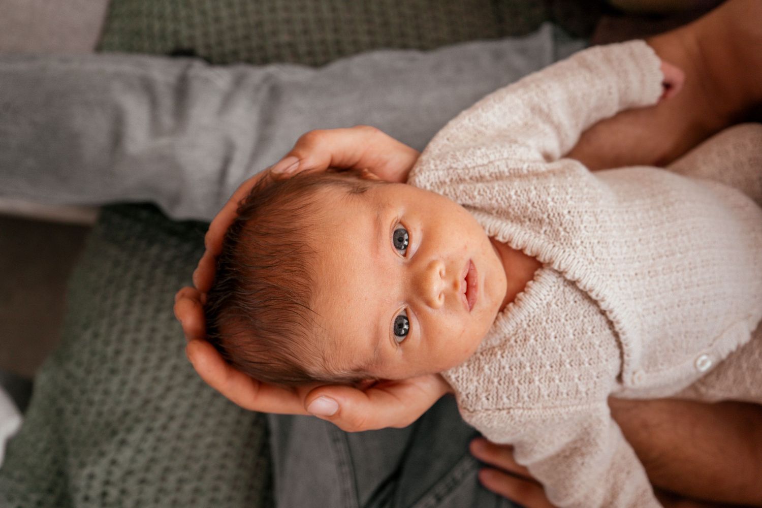Newborn photography session featuring gentle close-up shots in soft white knit clothing against neutral backdrop.