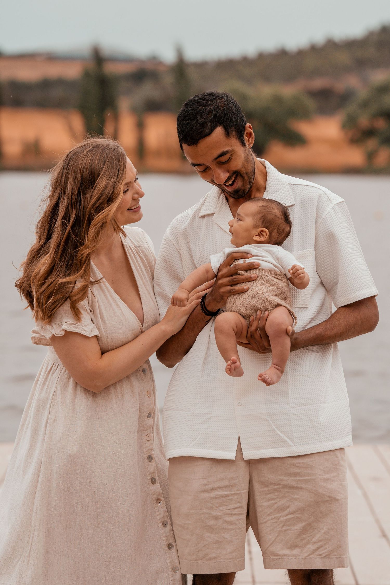 A family wearing coordinated white outfits poses playfully by a lake during a photo session.