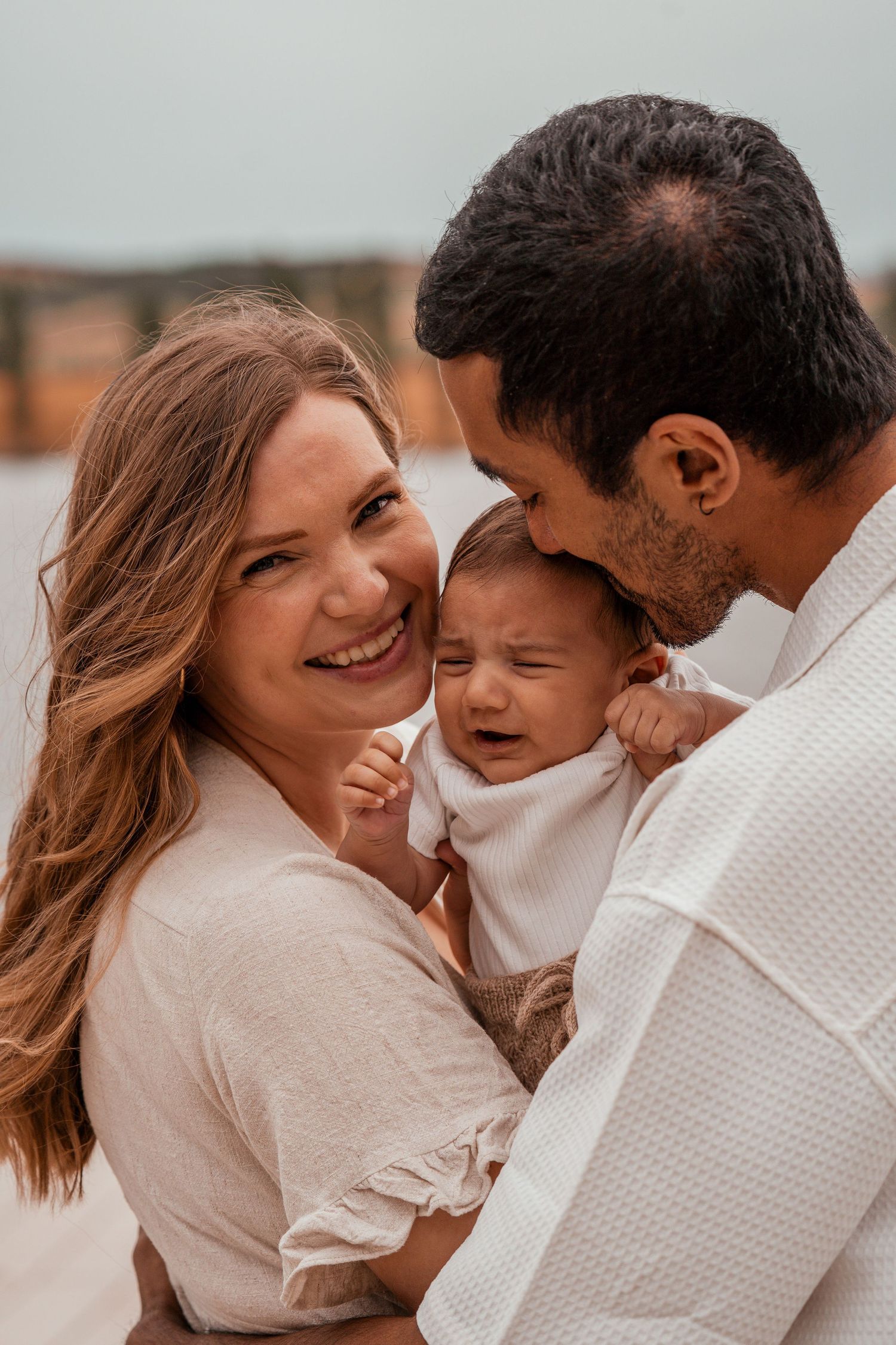 Candid moments of a family laughing and embracing while wearing matching white outfits outdoors.