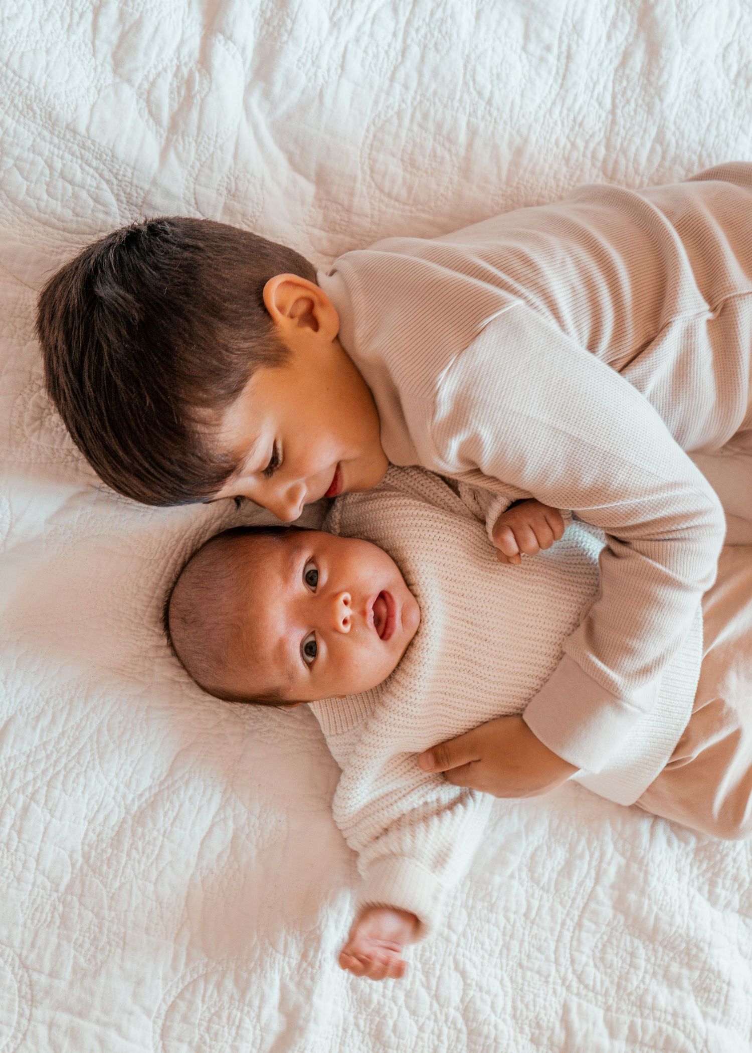 A small child in white sleepwear lies on soft white bedding in various playful poses.
