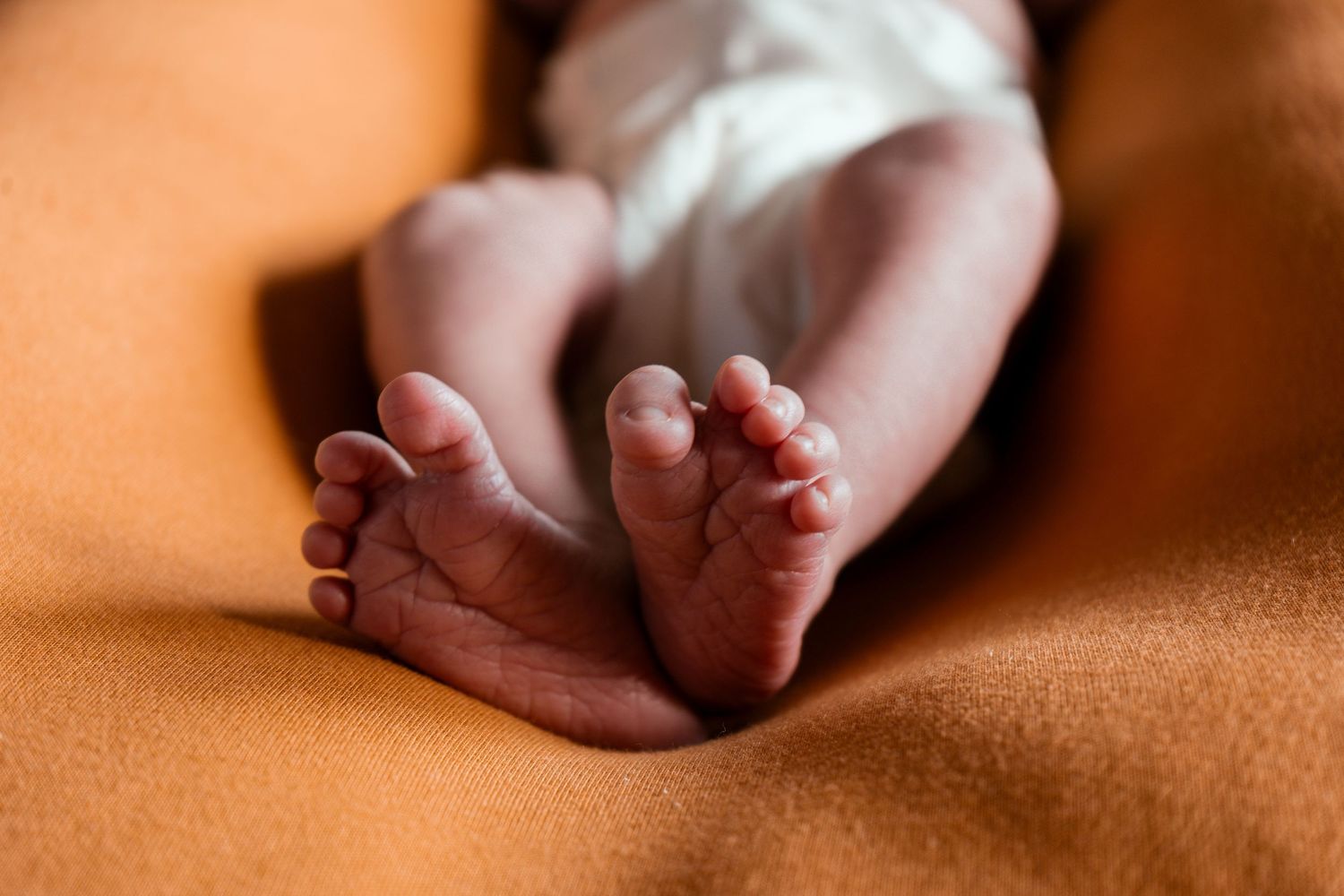 Close up of tiny newborn baby feet against an orange background.