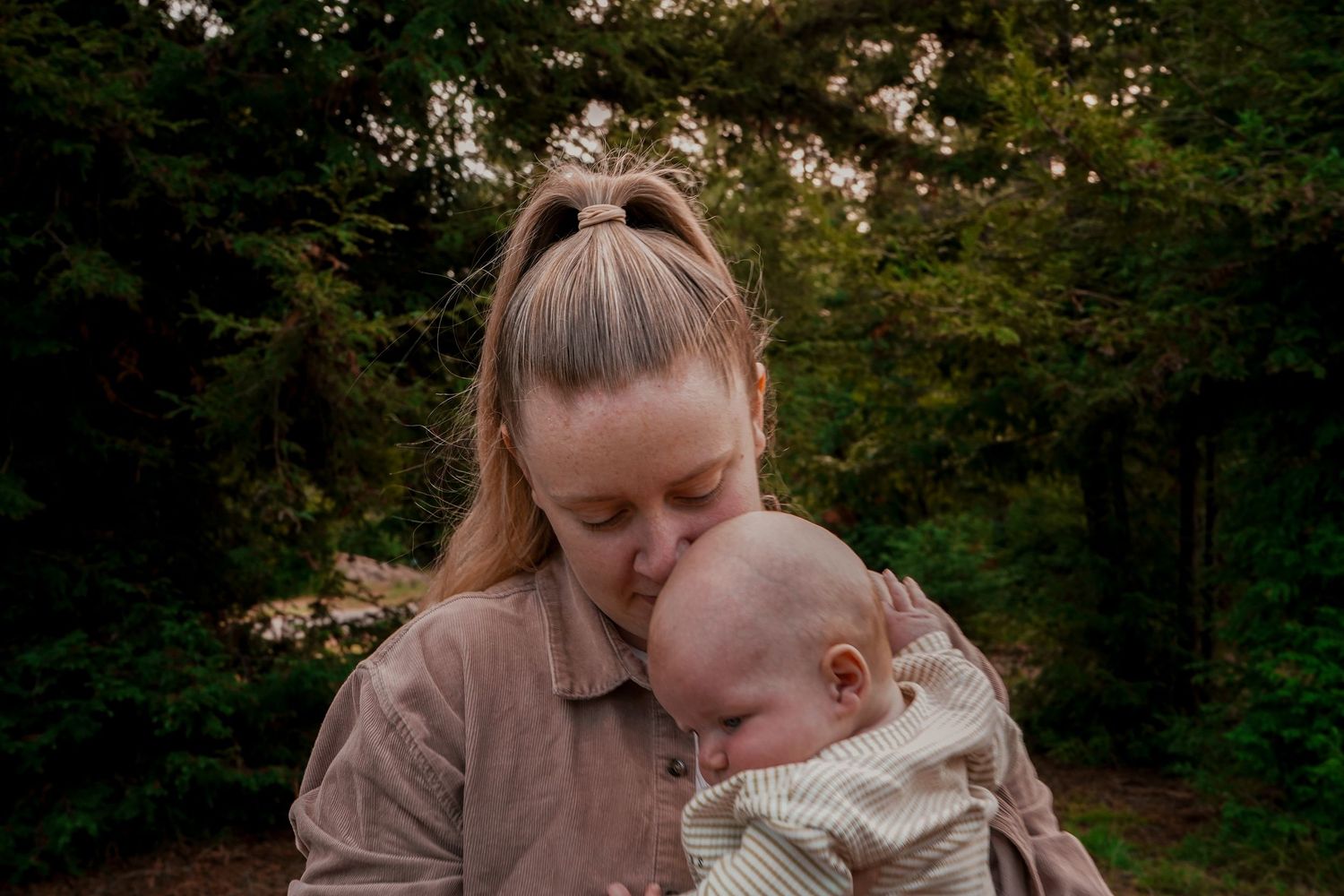 Tender moment captured outdoors with parent and baby in soft lighting.