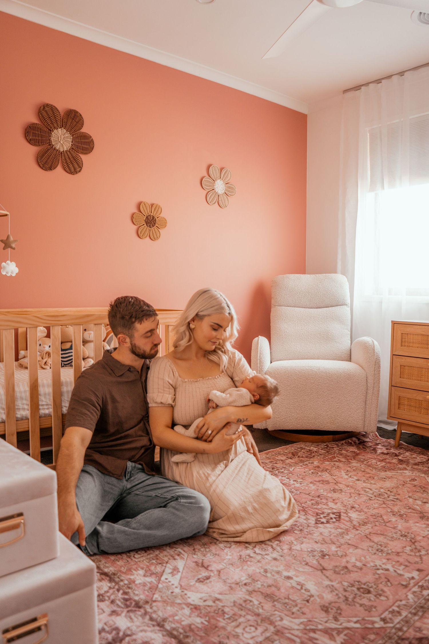 A cozy nursery scene with coral walls decorated with flower art and a comfortable white glider chair.