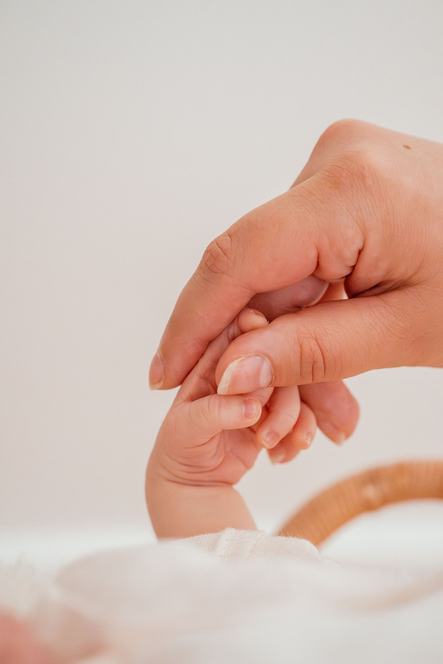 Close-up shot of a baby's tiny hand reaching up to touch an adult's hand against a soft white background.
