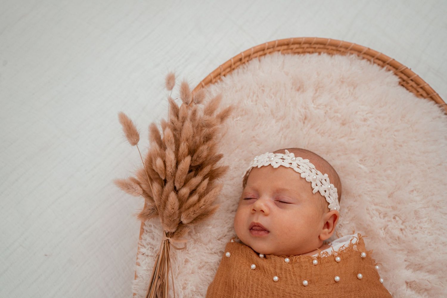 A sleeping newborn baby wearing a white headband rests peacefully on soft pink fabric.