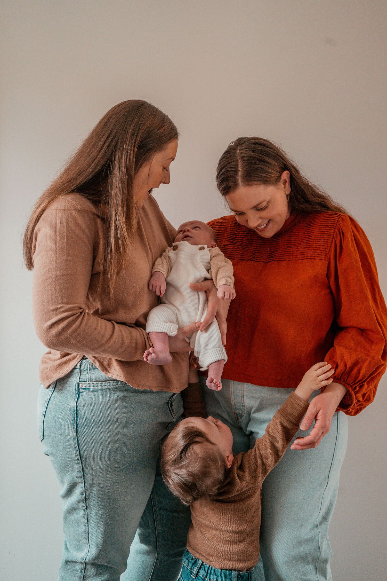 Two people in casual sweaters share a joyful moment with two small children in a warm-toned indoor setting.
