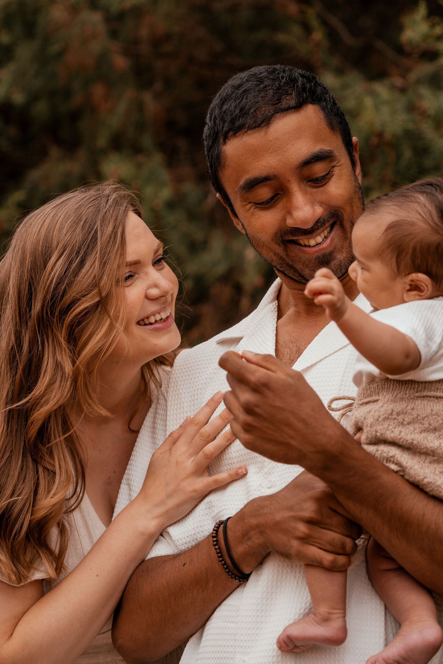 A joyful family shares a tender moment together outdoors, laughing and bonding with their young baby.