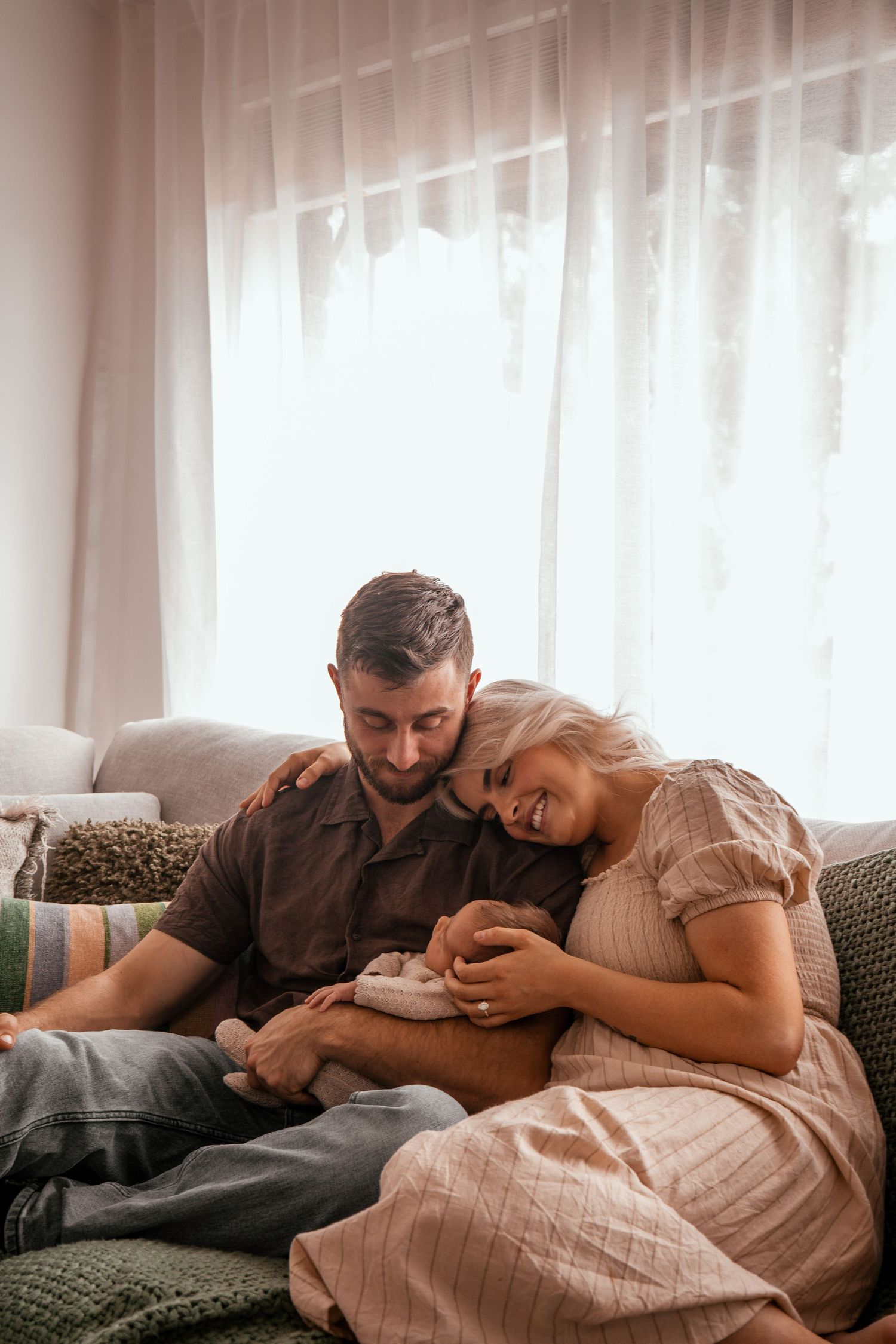 A tender moment shared on a green couch near sunlit sheer curtains in a bright room.