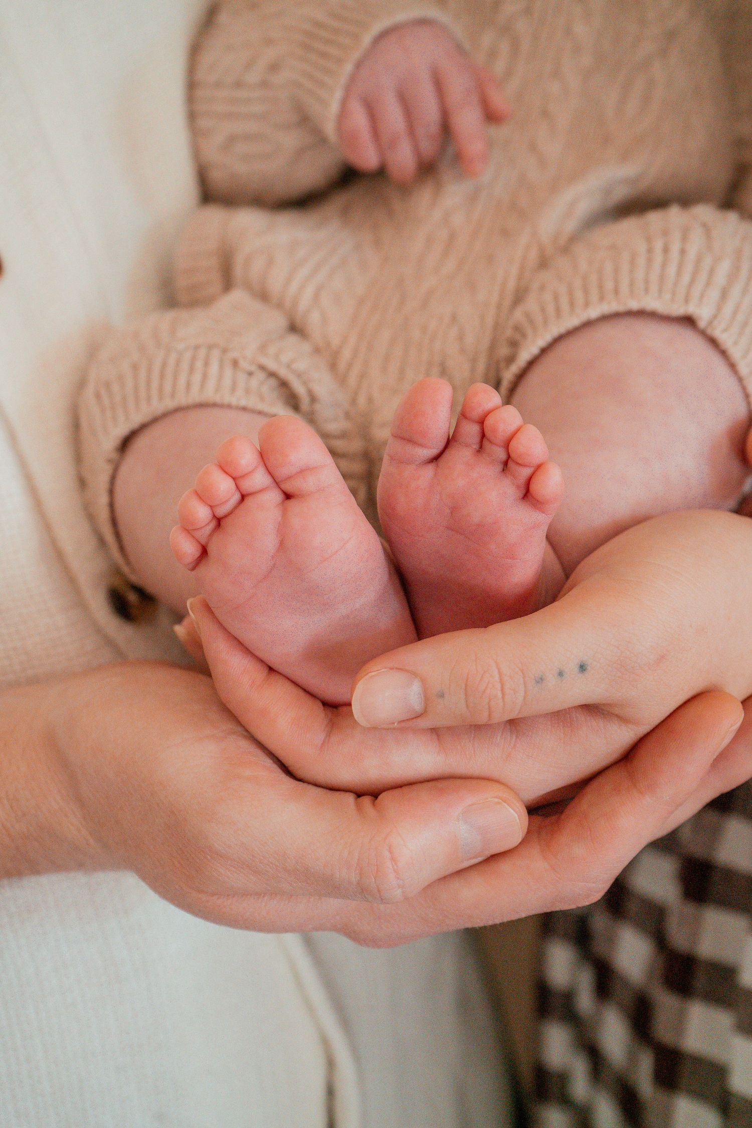 Adult hands gently cradle tiny baby feet in a tender moment against soft beige knit fabric.