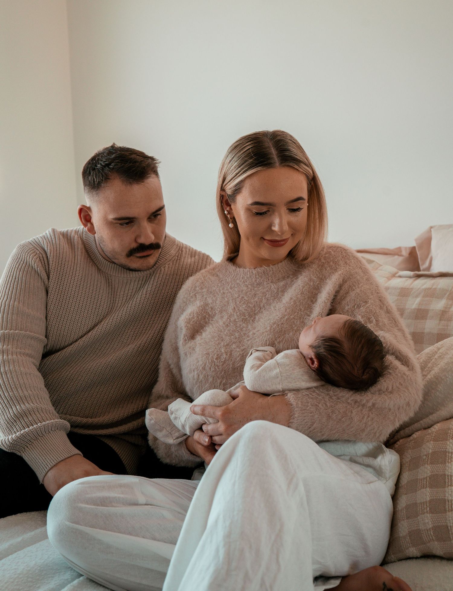 Family shares intimate moment on couch while cradling their newborn in soft neutral-toned clothing.