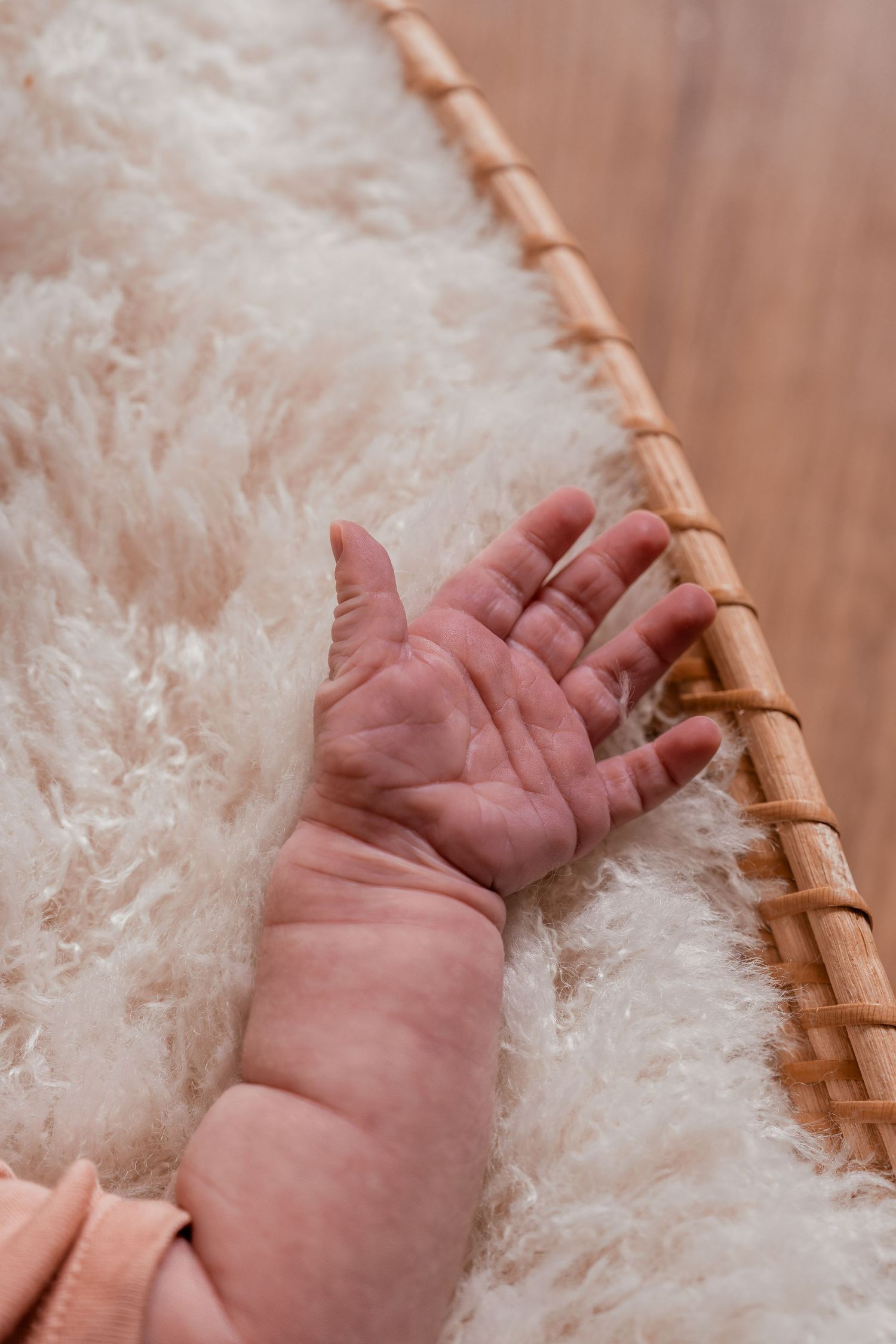 Close-up shots of a tiny baby's hand resting on soft white fluffy fabric with a wooden accent visible.