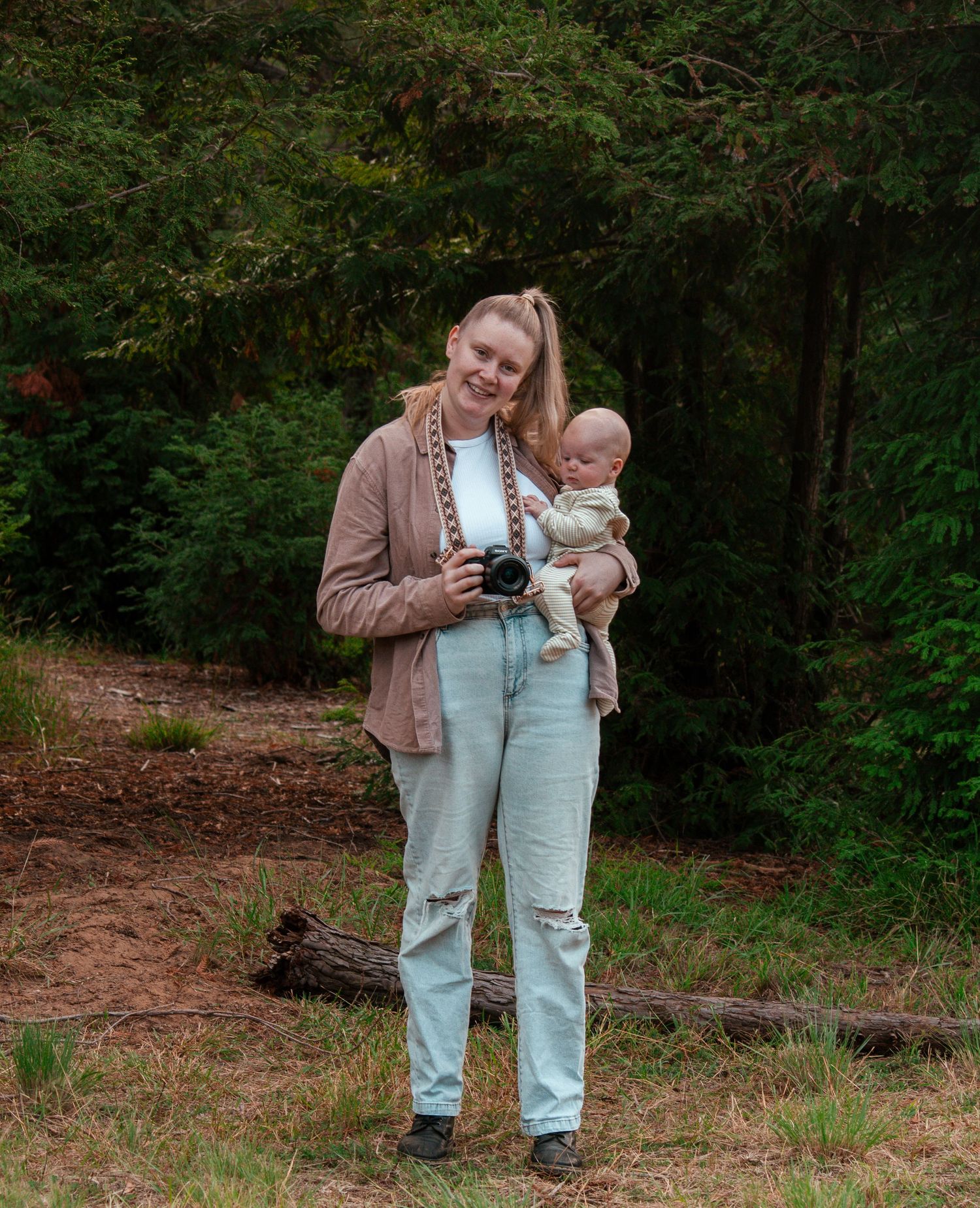 Parent and infant stand together in a forest setting while holding a camera.