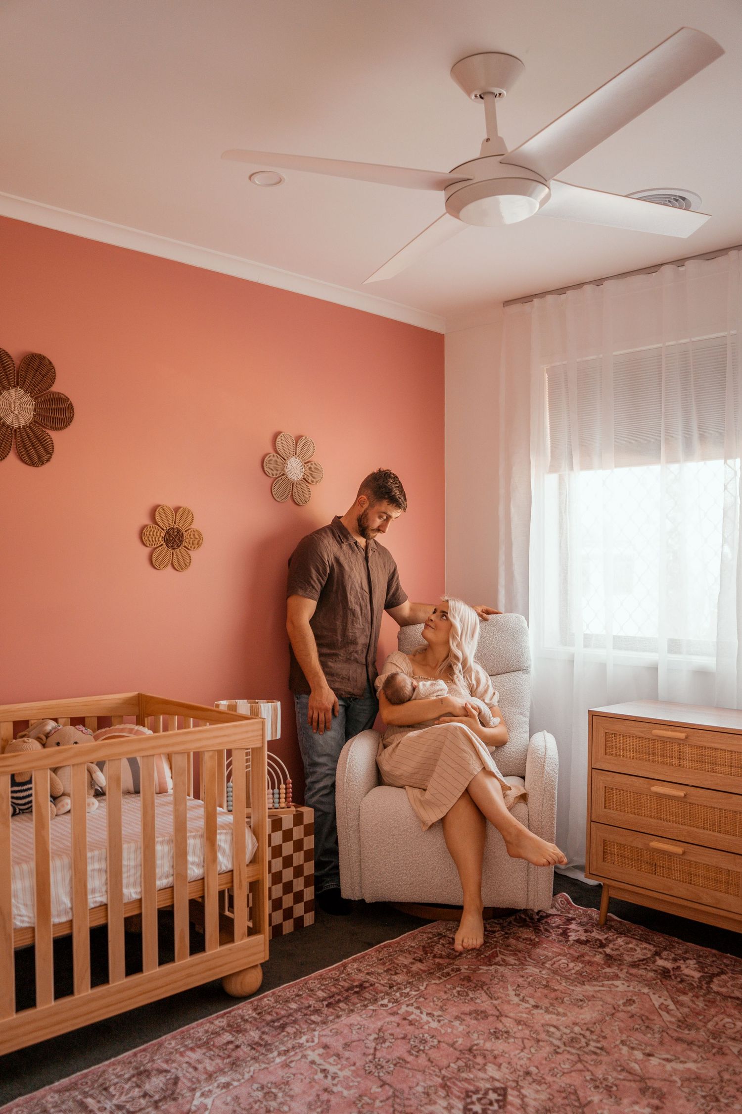 A cozy coral-colored nursery with wooden furniture, floral wall decor, and a ceiling fan.