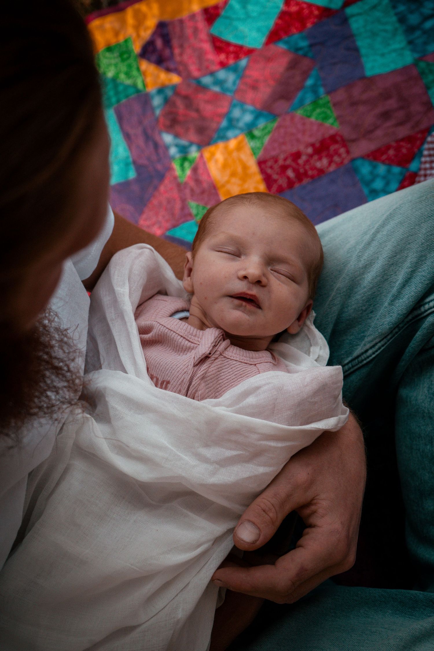 Baby resting against colorful patchwork quilt with hands gently supporting their head.