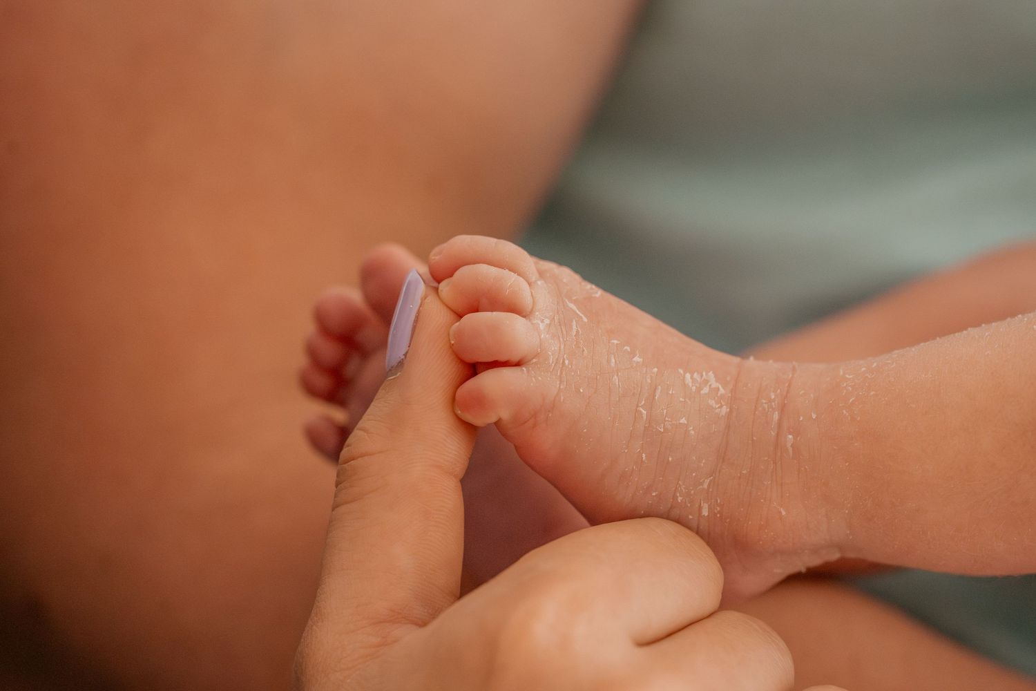 Close up of hands gently holding and massaging a baby's tiny foot during an infant massage session.