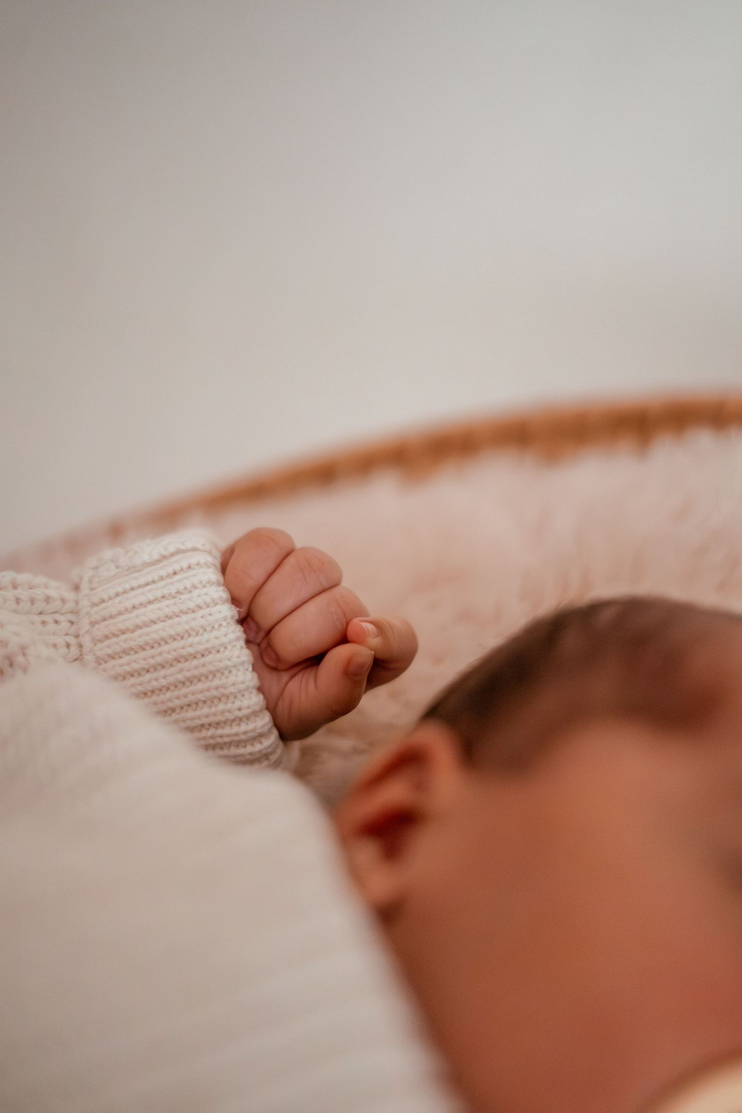 Close-up of a tiny baby hand grasping a white knitted sweater while sleeping peacefully.