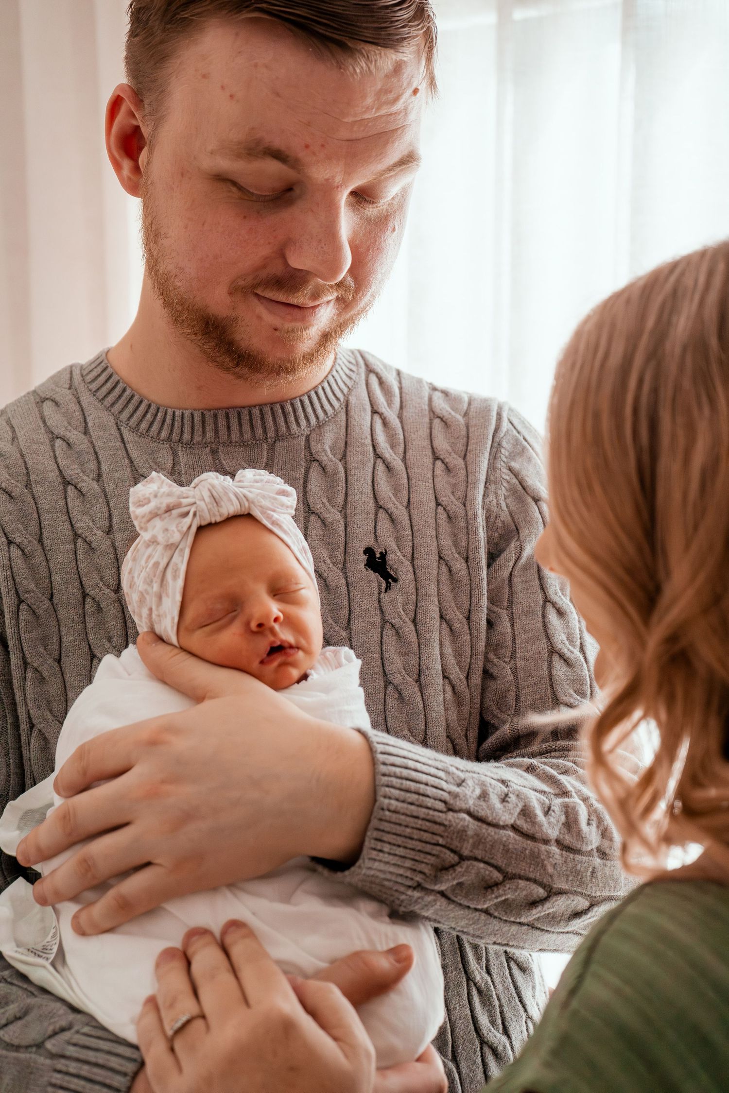 Parents in matching sweaters hold their newborn baby in a series of tender moments at home.