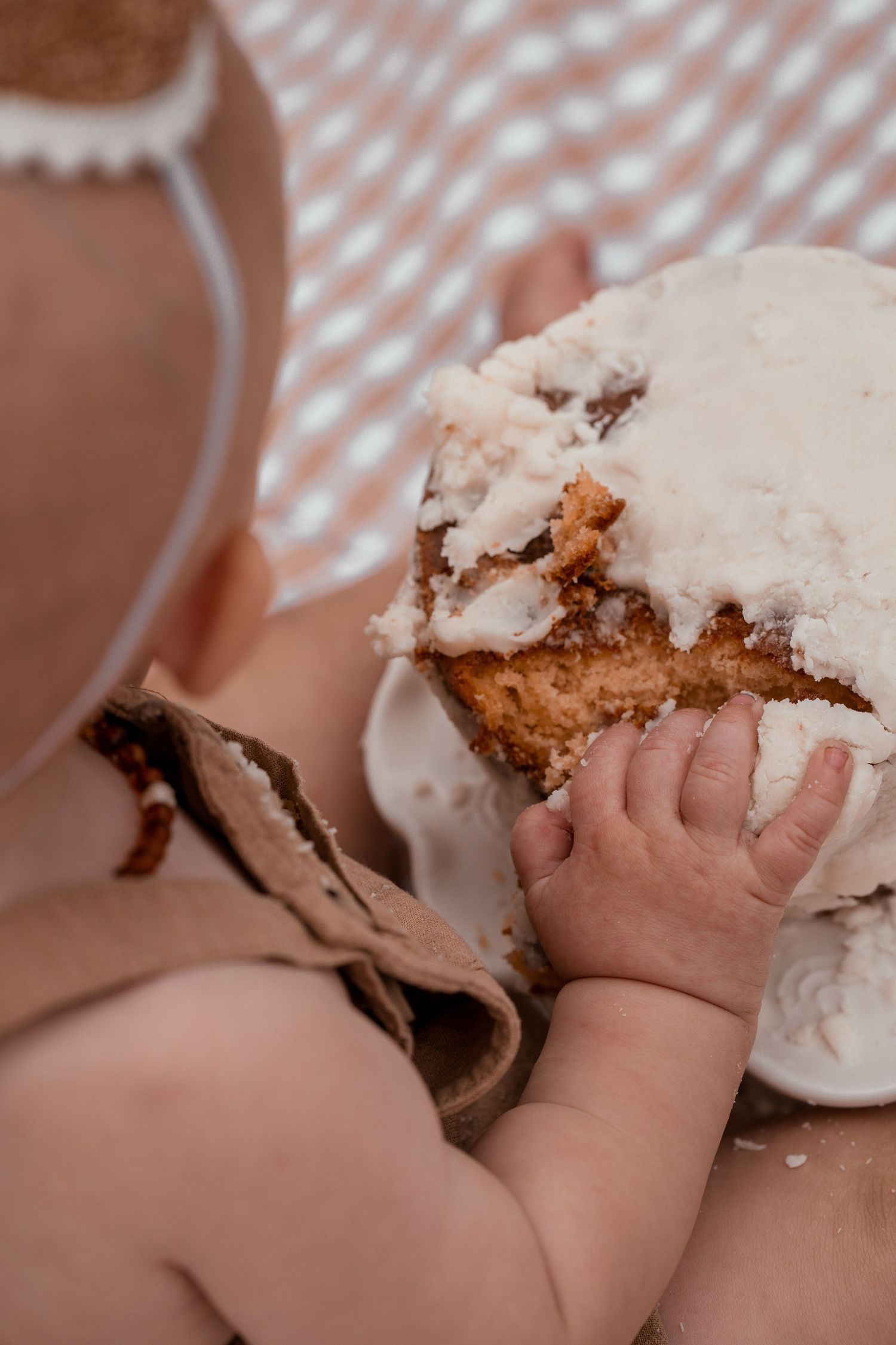 Baby's hand reaching for a powdered donut or pastry on a checkered tablecloth.