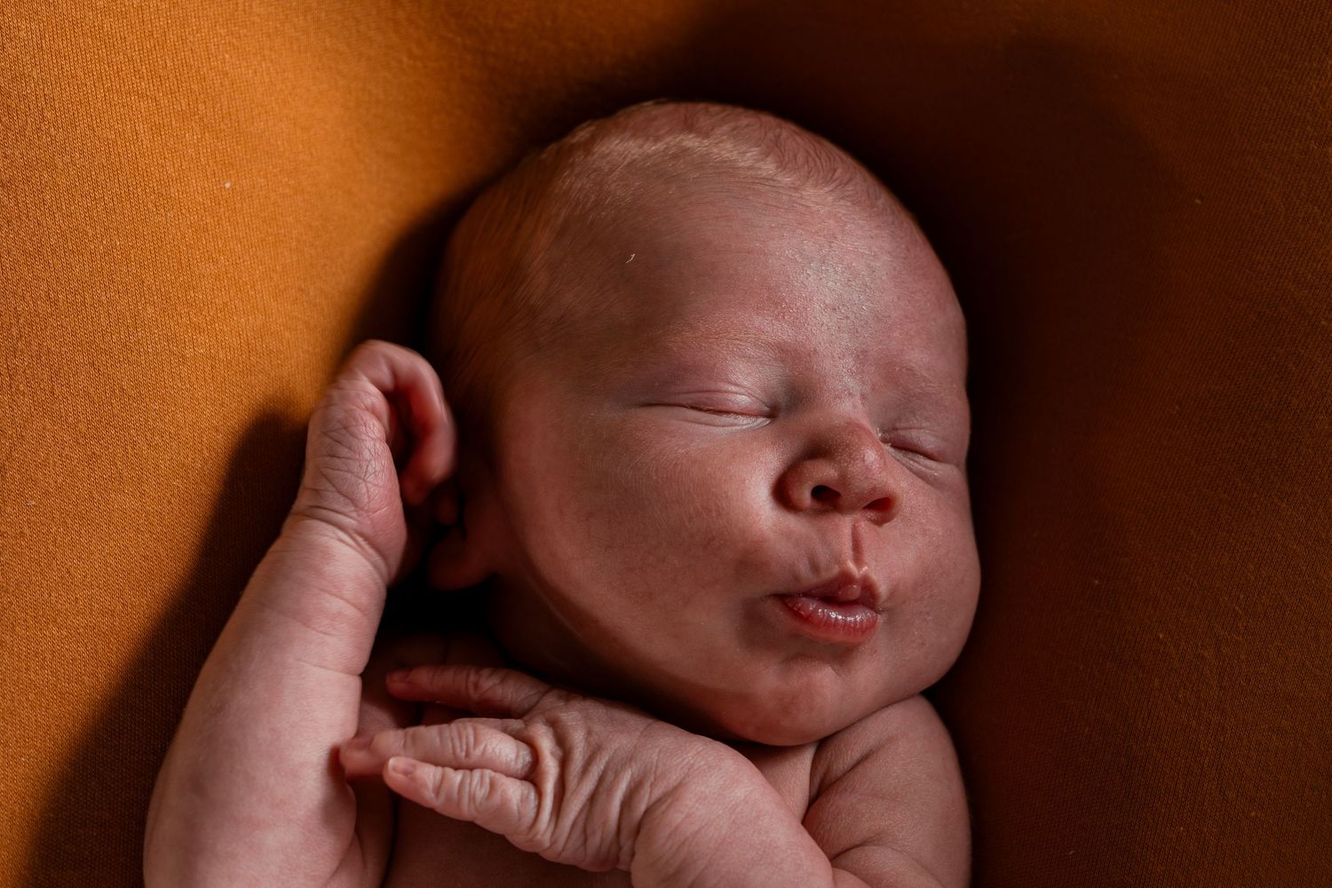 Peaceful sleeping newborn baby resting on orange background in gentle lighting.