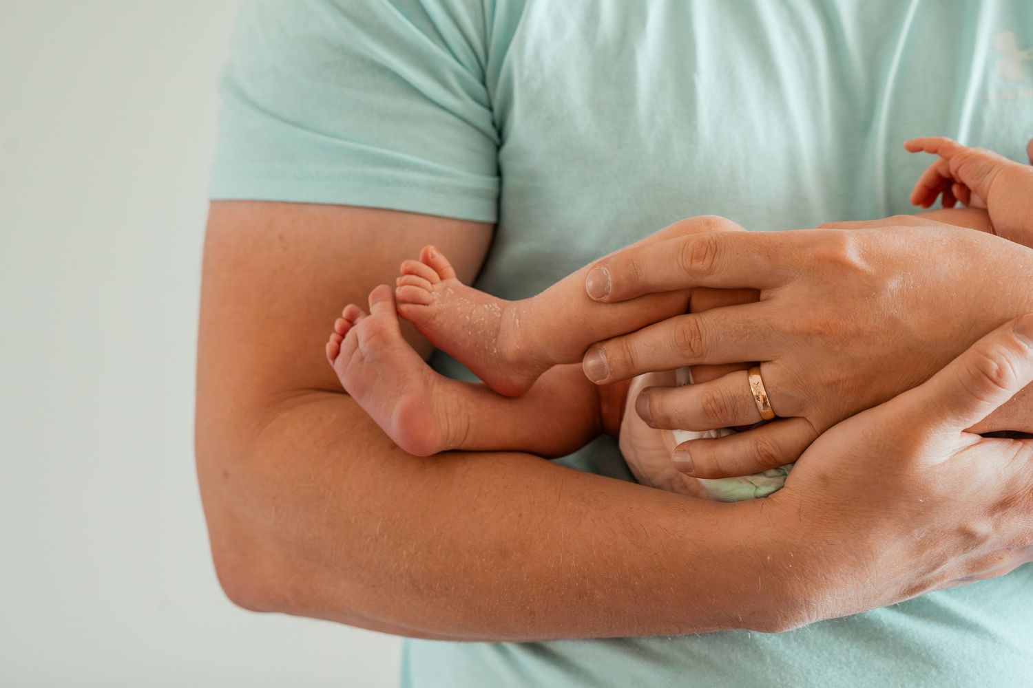Newborn baby feet resting in adult hands while wearing mint green clothing.