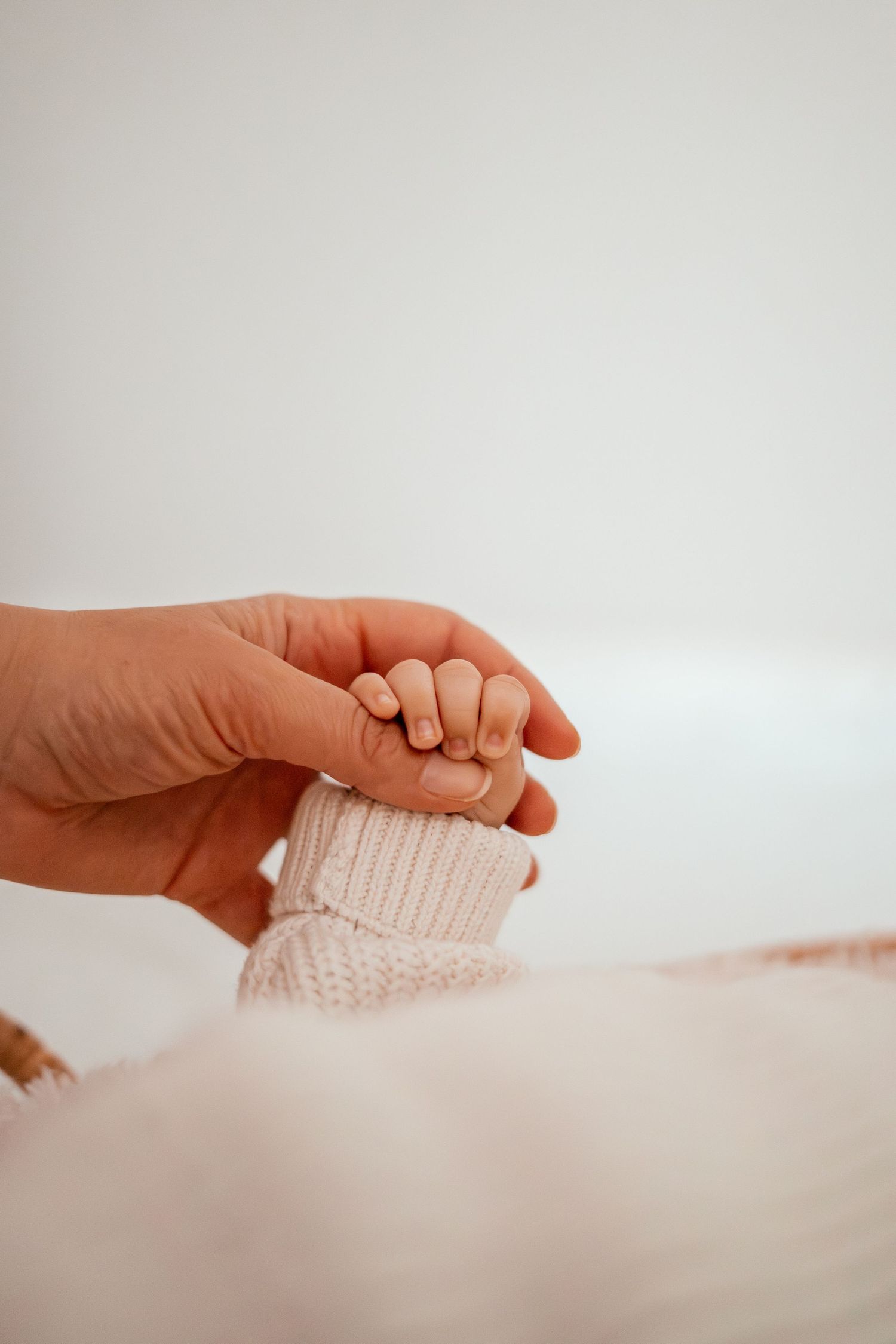 Close-up of hands gently holding a soft white knit fabric against a light background.