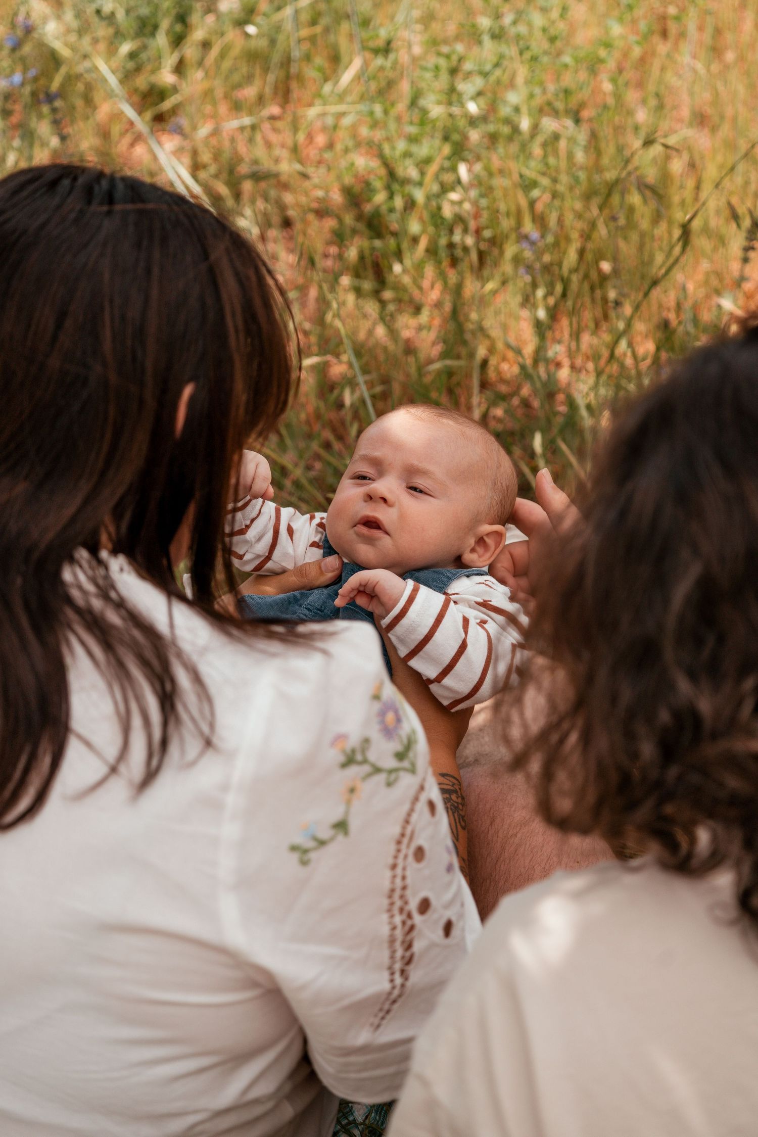 A small infant in a striped outfit being cradled outdoors against a natural brown background.