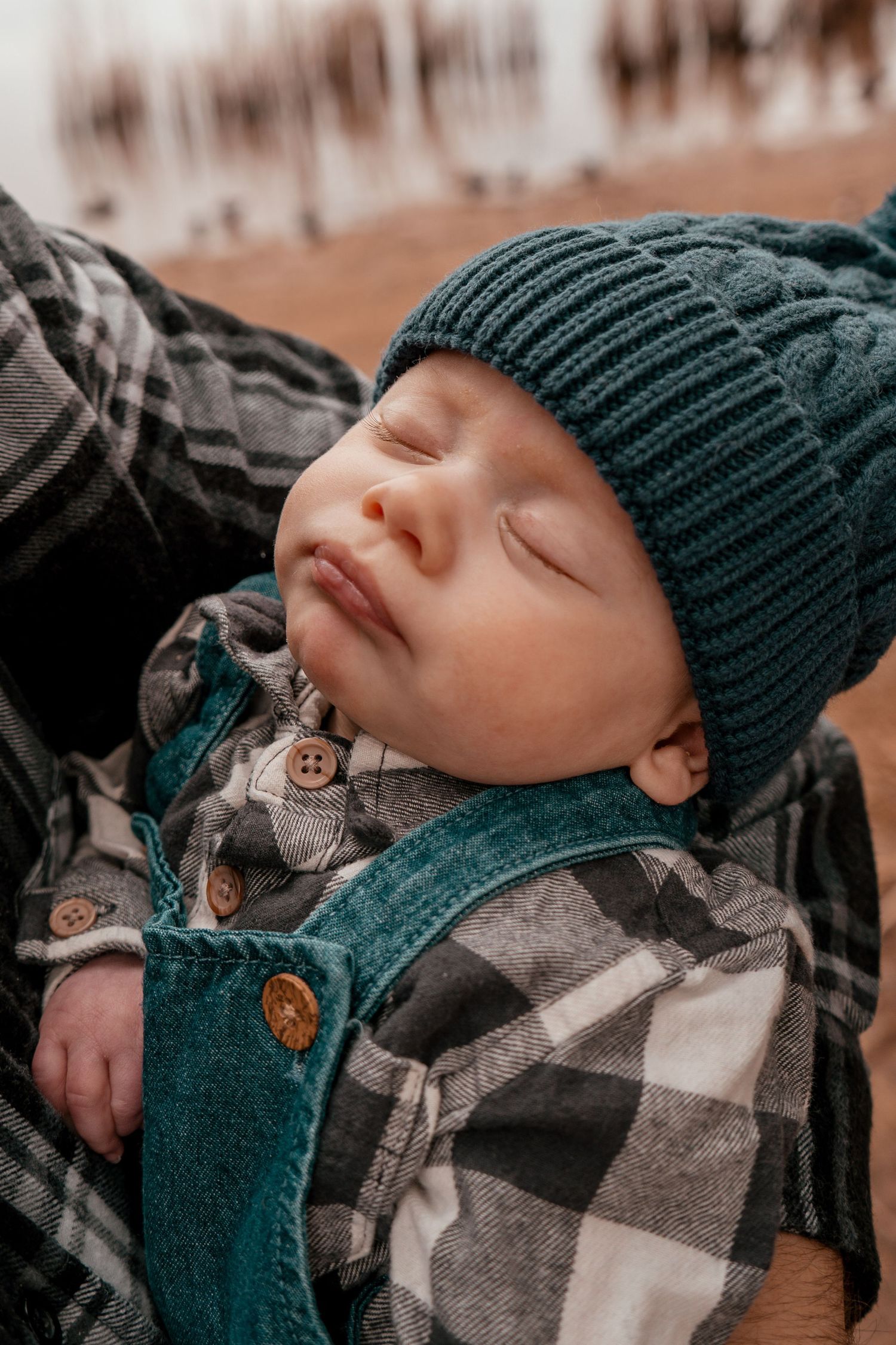 A baby in a dark knit beanie and plaid shirt sleeps peacefully in a series of close-up photos.